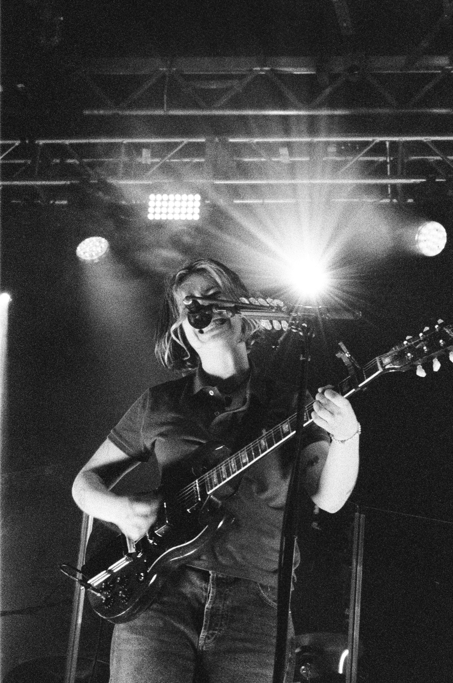 Black and white concert photo of a smiling guitarist performing on stage under bright spotlights.