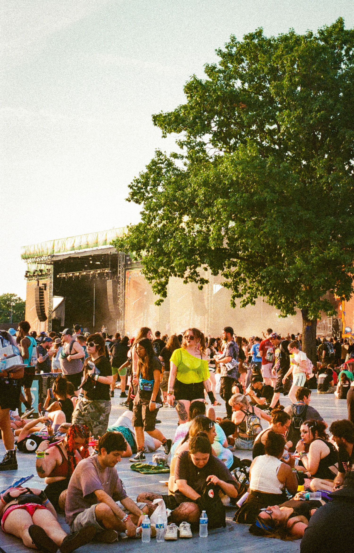 Festival attendees sit and stand near a large outdoor stage during golden hour sunset.