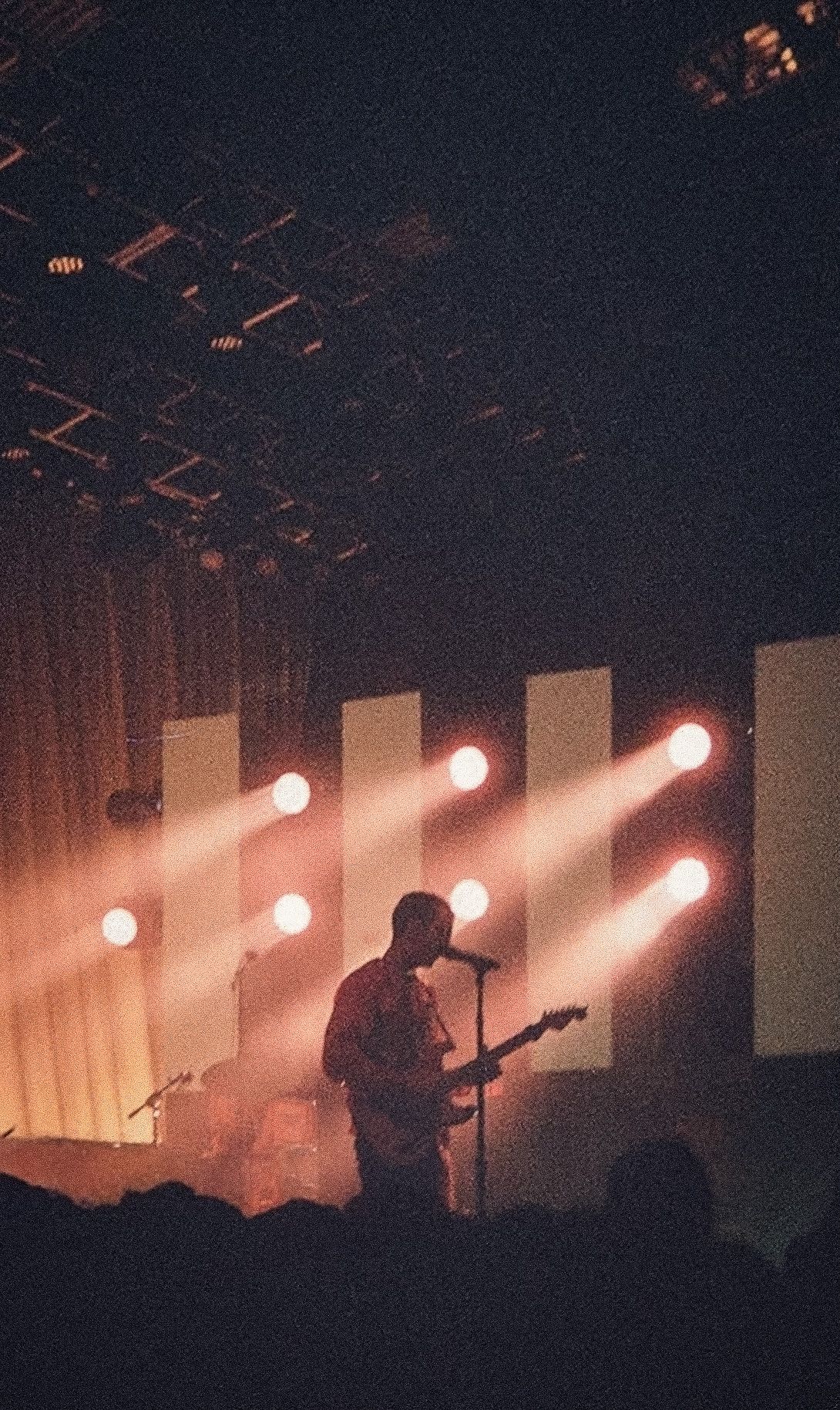 Guitarist performs solo on a dark stage illuminated by warm orange row of spotlights.