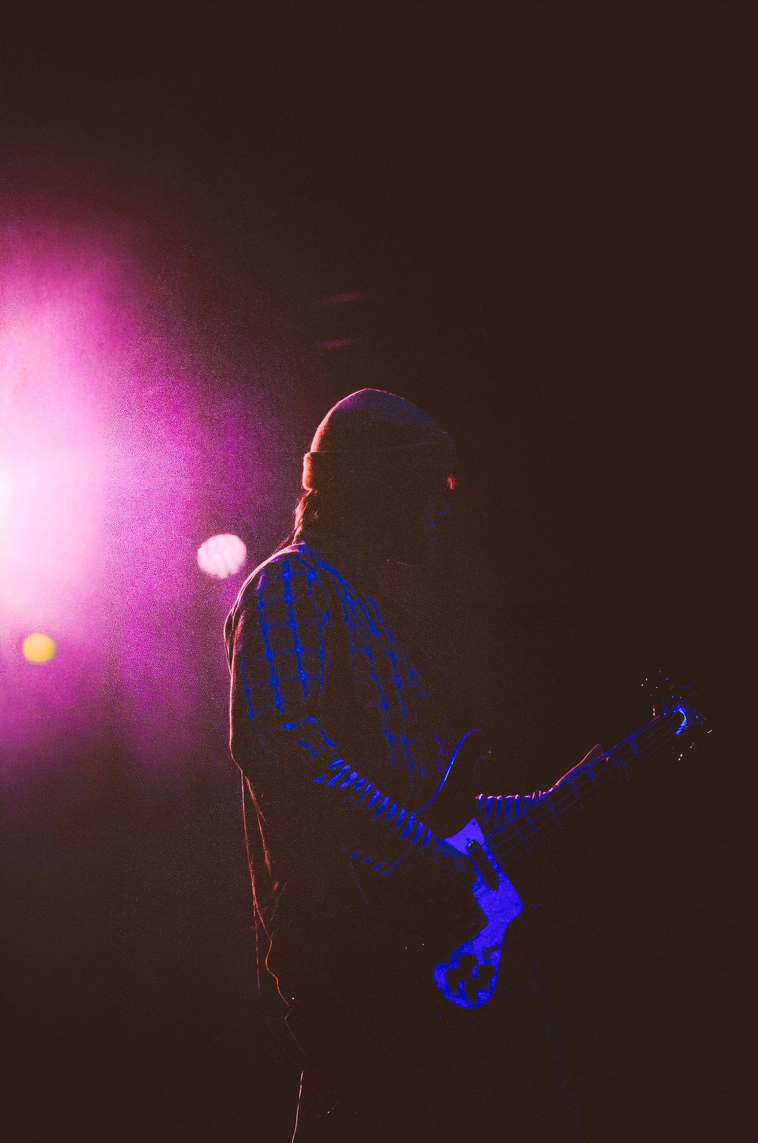 A guitarist performs on stage bathed in dramatic purple and blue stage lighting during a live concert.