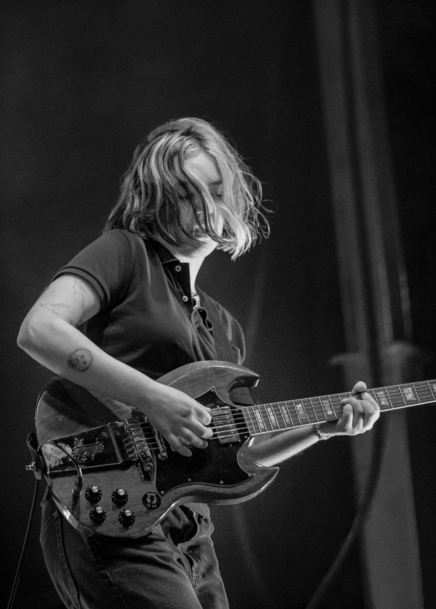 Black and white photo of a young guitarist with flowing hair playing an electric guitar on stage.
