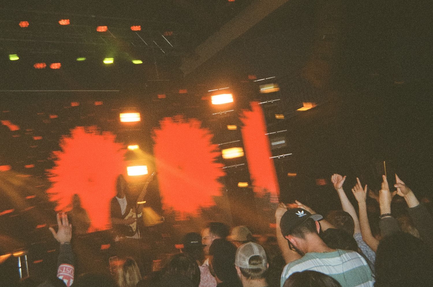 Blurred motion shot of concert crowd with hands raised under dramatic red flare stage lighting.