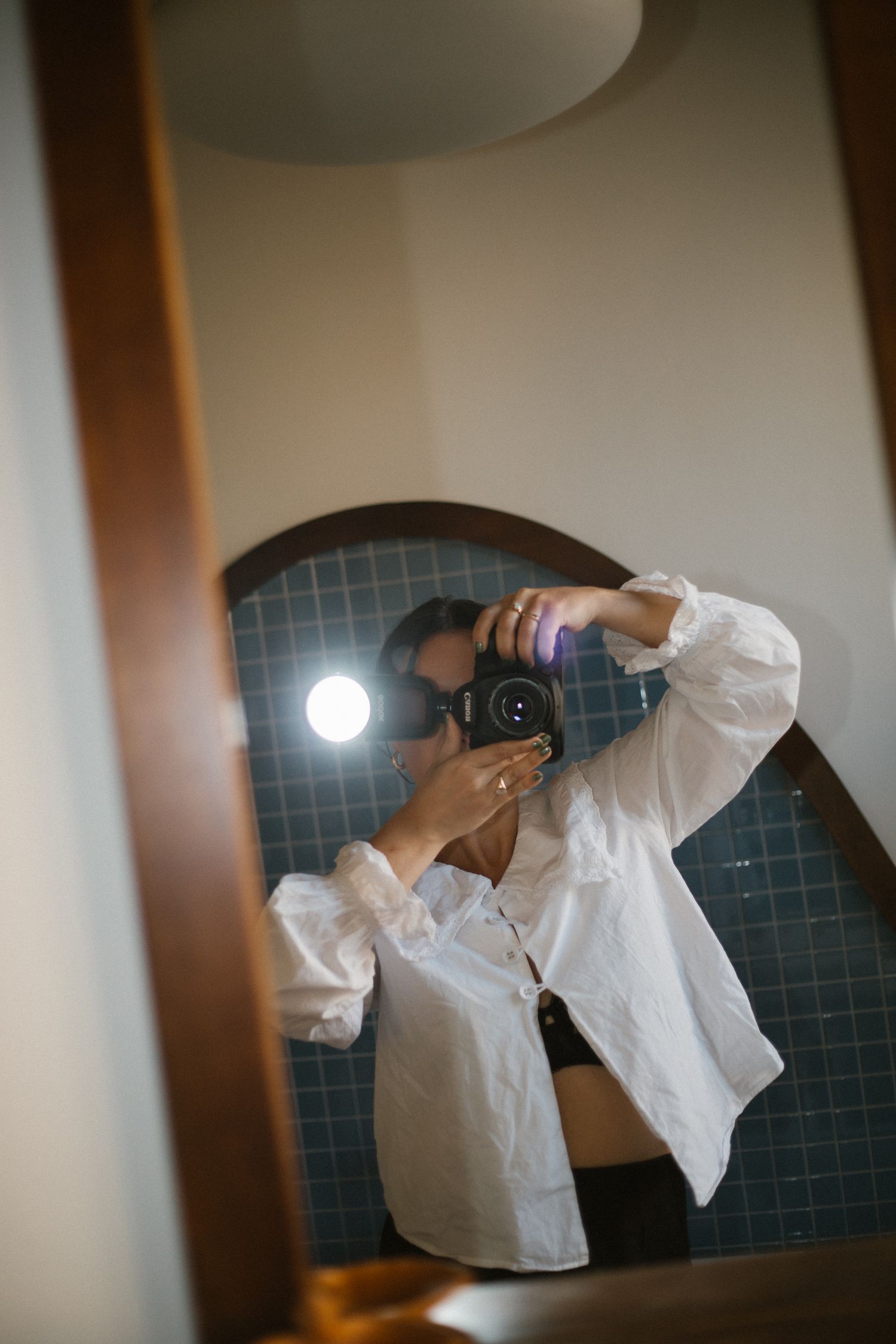 Photographer capturing mirror selfie with flash in tiled bathroom reflection.