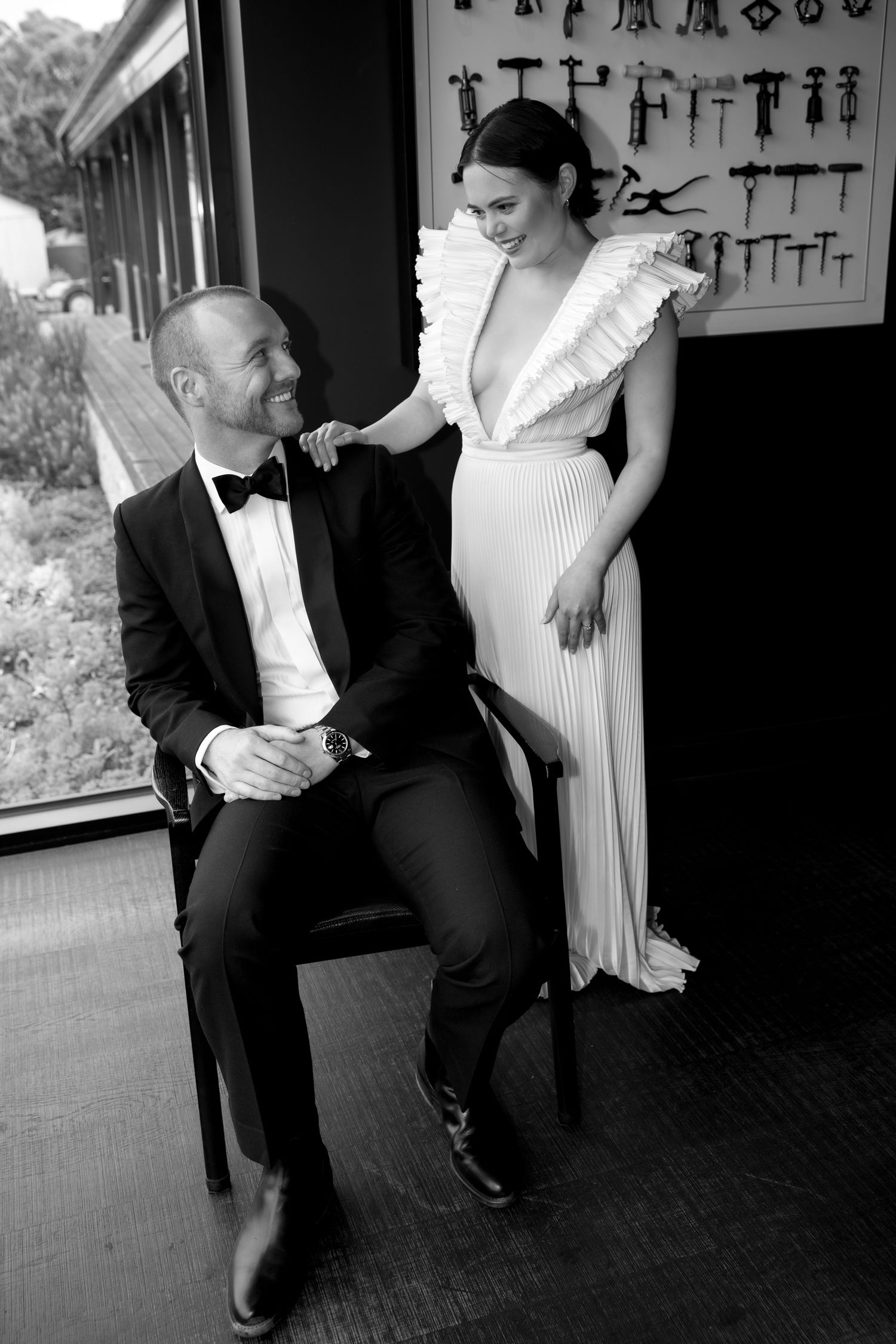 Black and white photo of groom seated smiling up at bride in ruffled wedding dress.