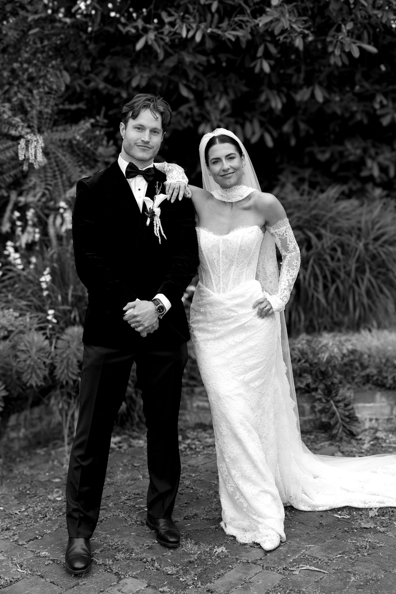 Black and white photo of bride and groom posing together in a garden on their wedding day.