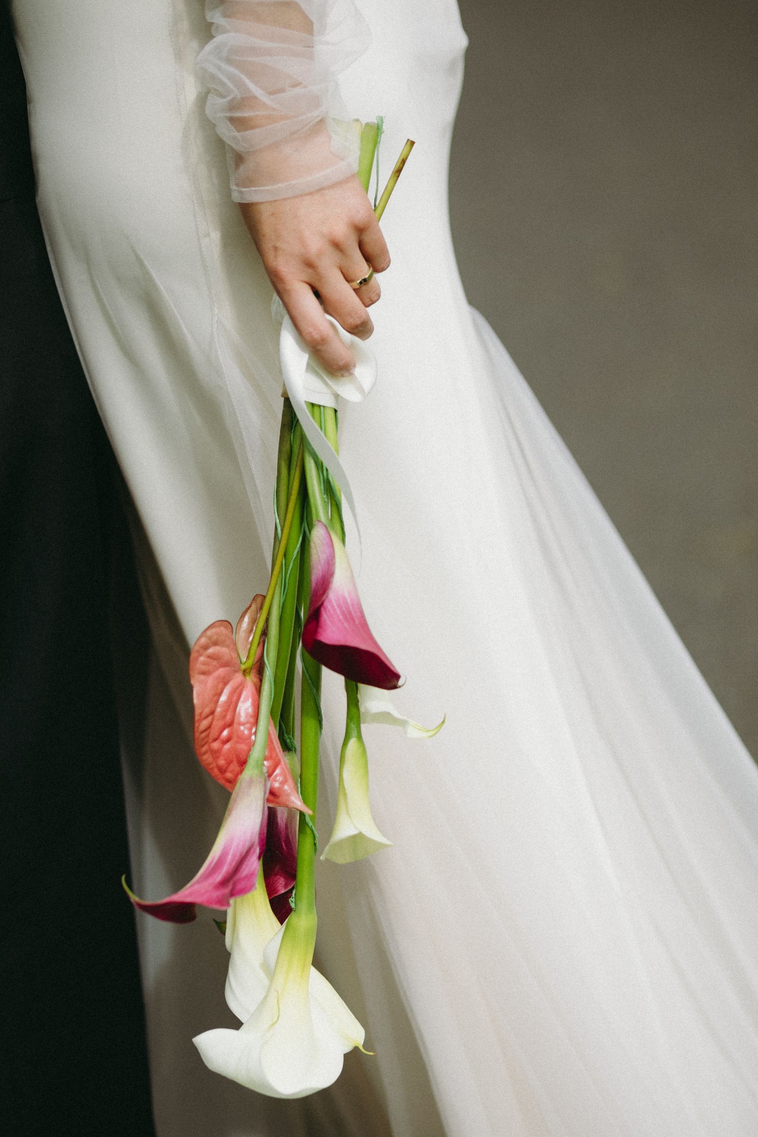Bride holding elegant cascading bouquet of white and pink calla lilies with anthurium in flowing gown.