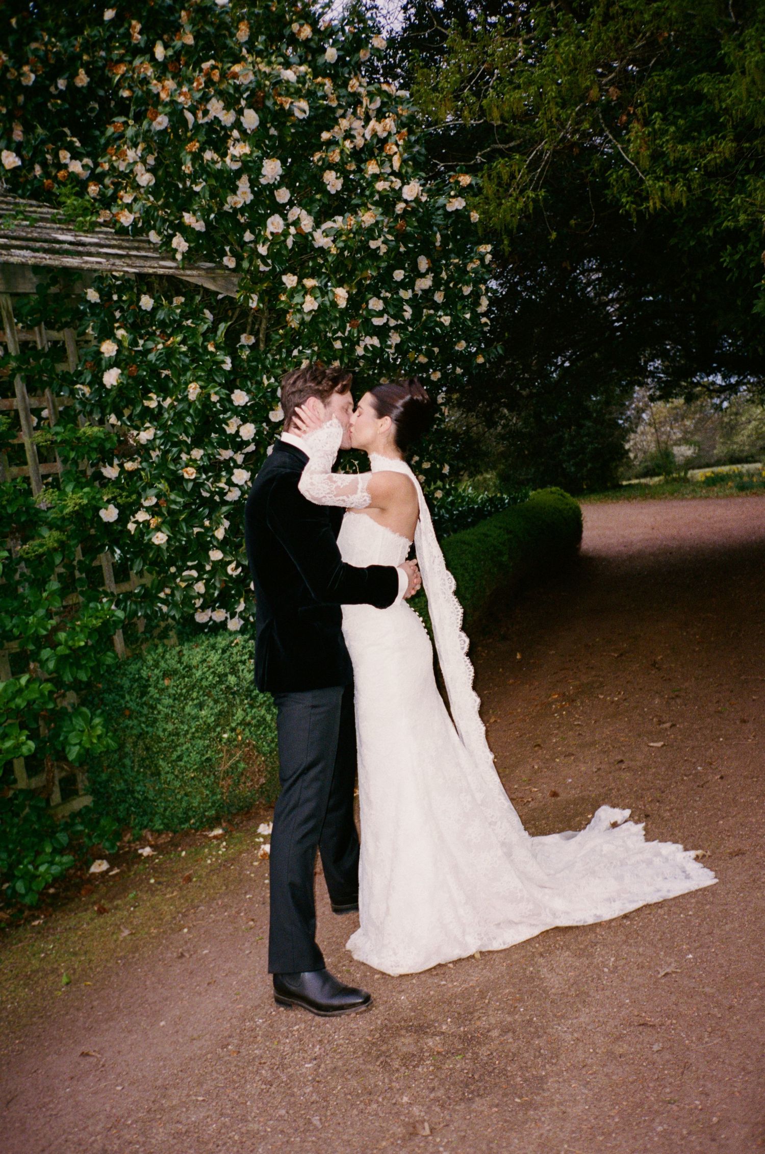 Bride and groom sharing a romantic kiss in a garden, surrounded by blooming roses and lush greenery.