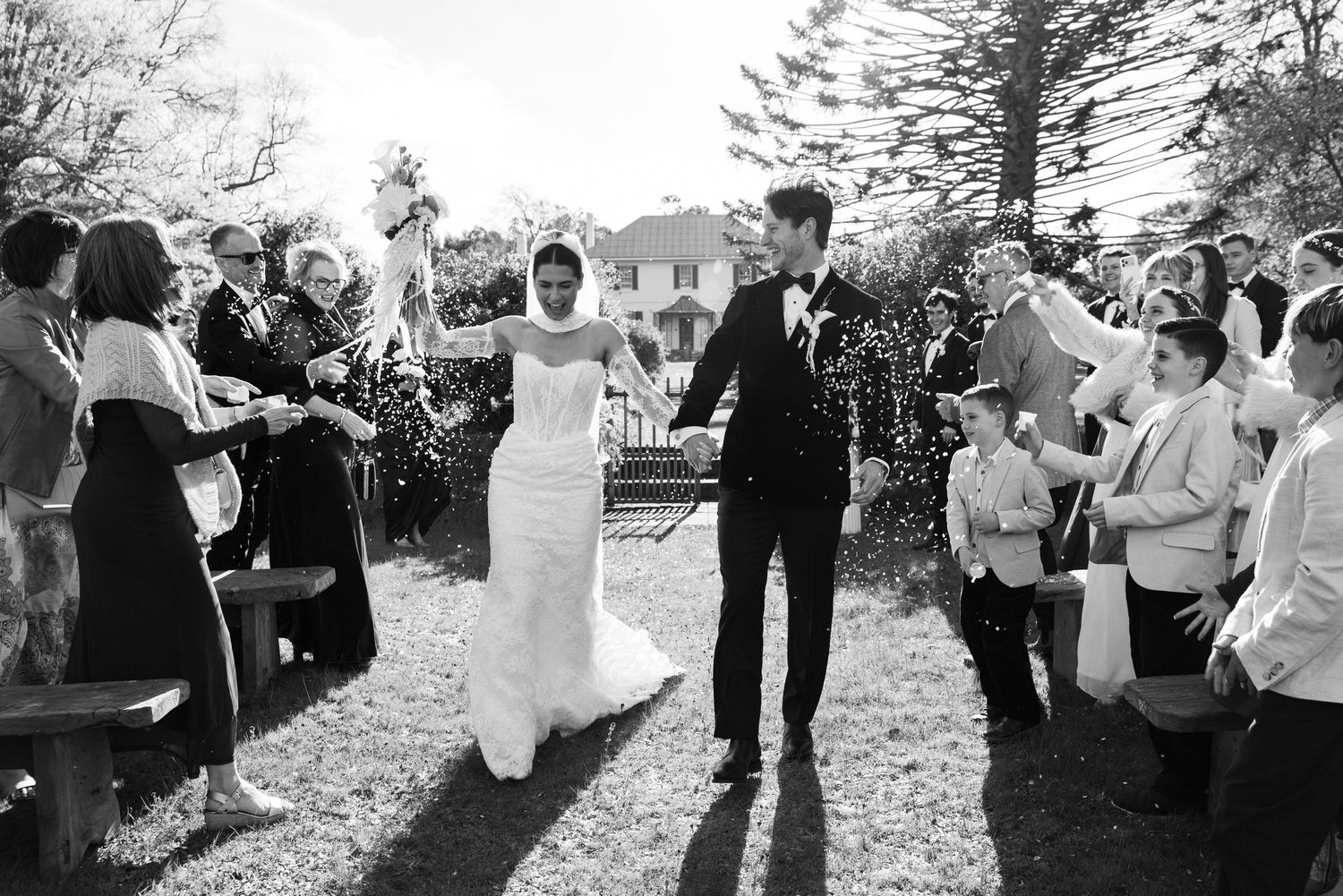 Newlyweds walk through confetti shower as guests celebrate their outdoor wedding ceremony.