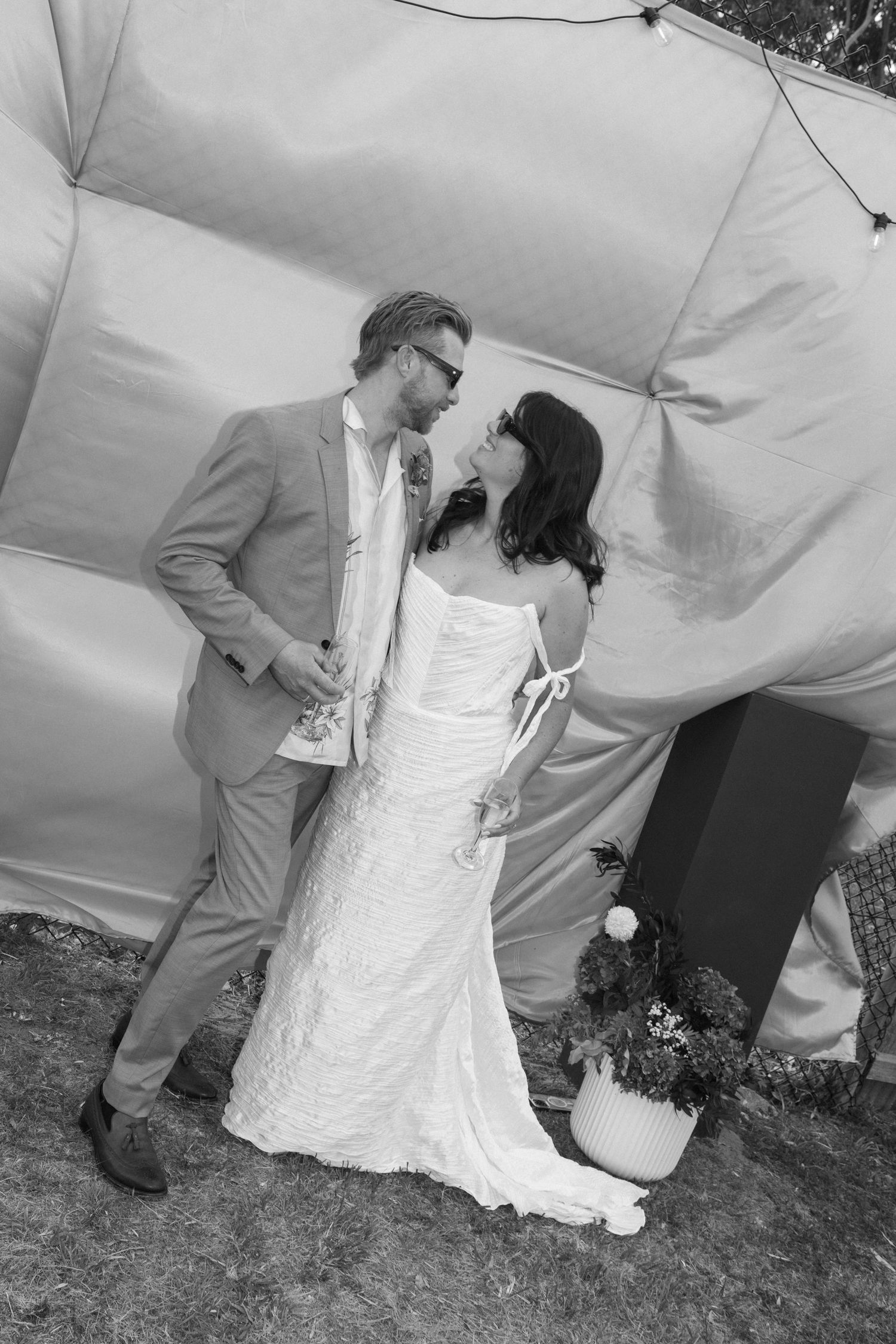 Black and white photo of a bride and groom sharing a romantic moment outside a tent at their wedding.