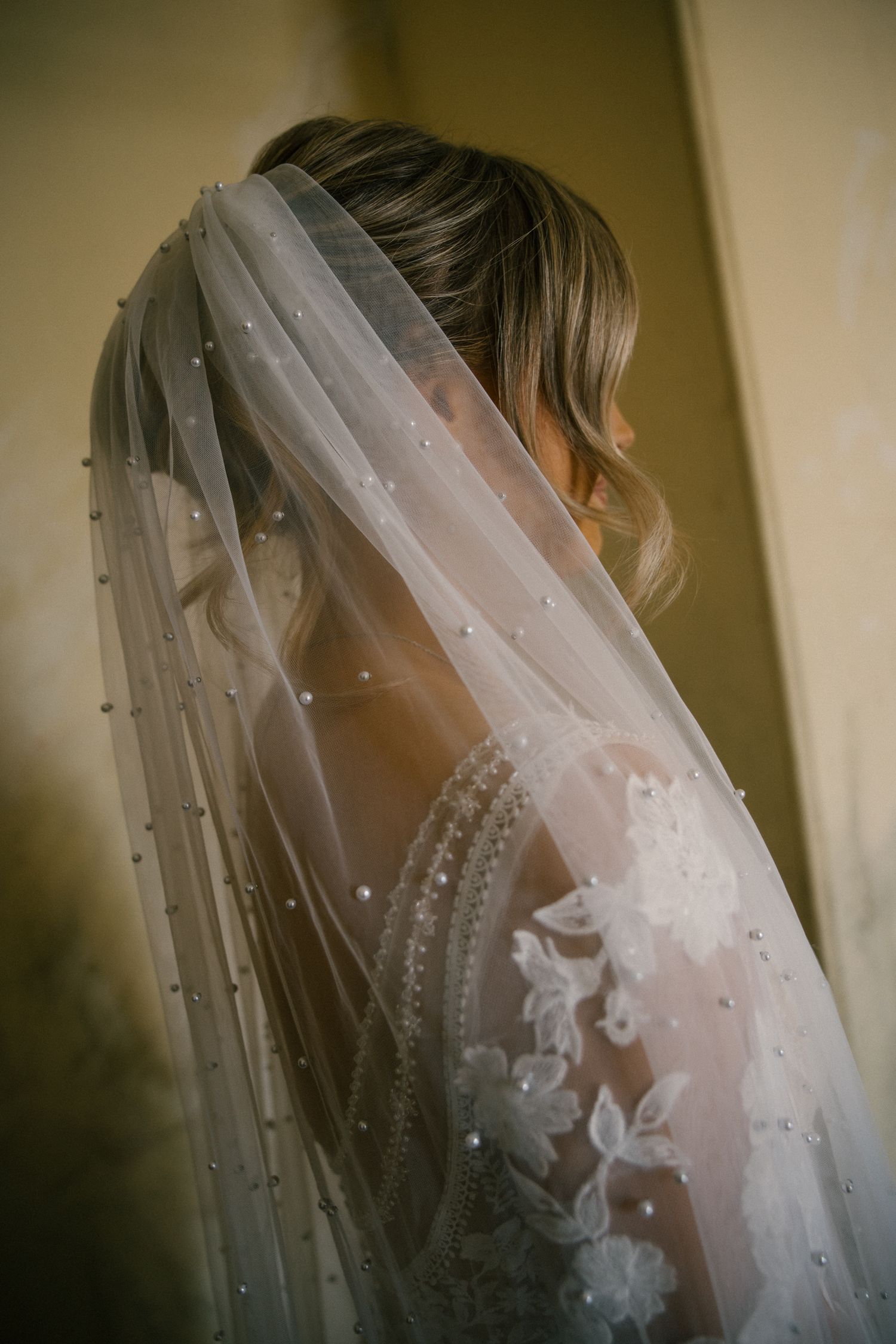 Close-up of bride wearing pearl-embellished lace wedding veil with floral applique details.