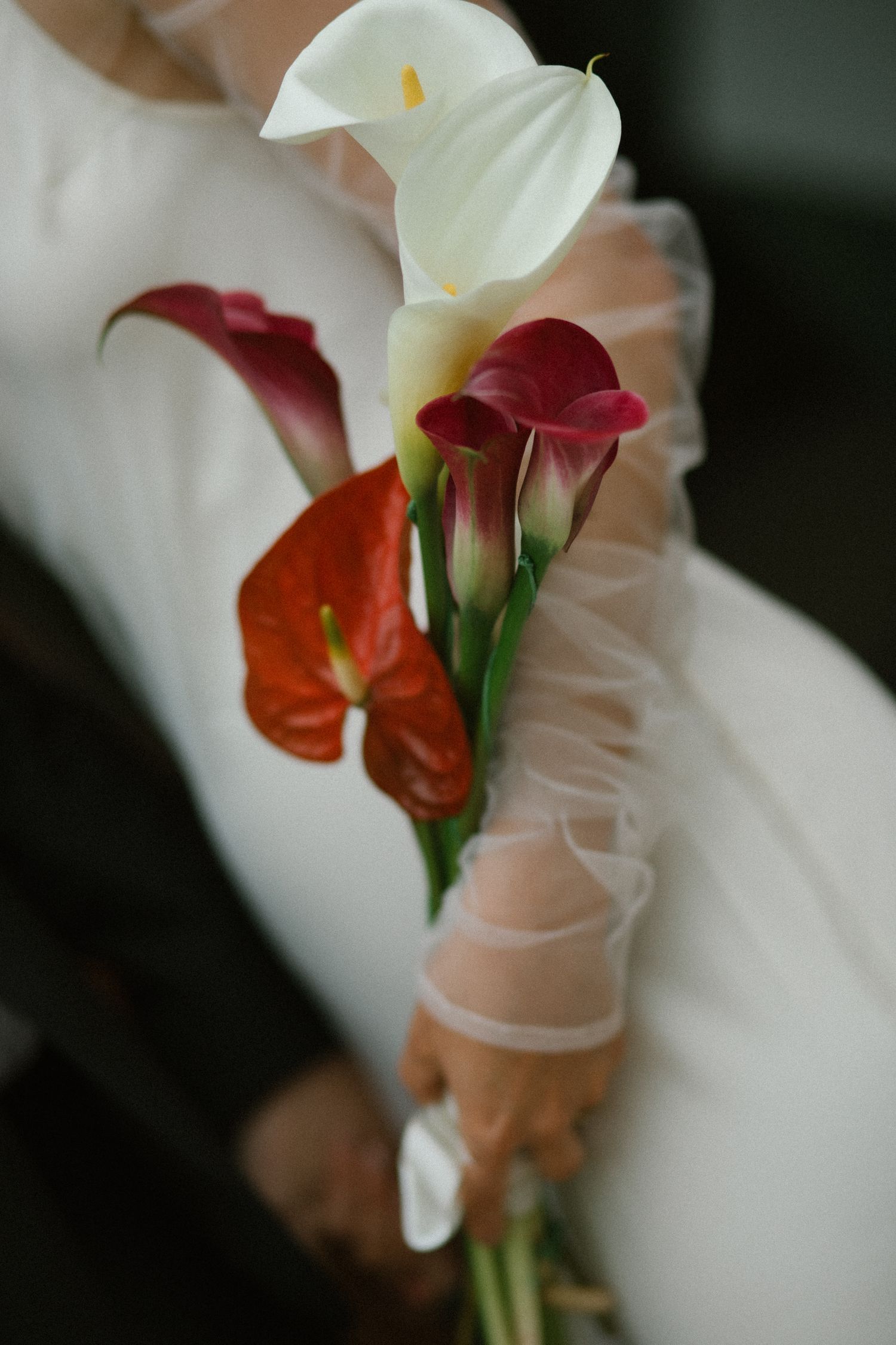 Bride holding elegant bouquet of white and red calla lilies with anthurium flowers.