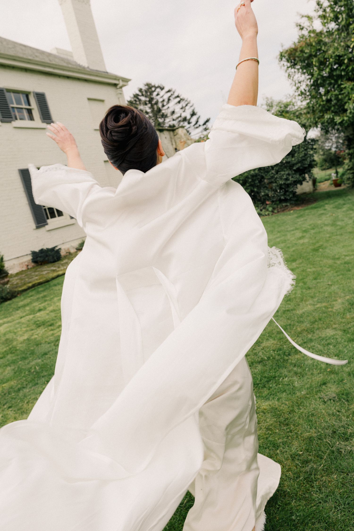 Bride in white gown twirls on green lawn with flowing dress and upswept hair.