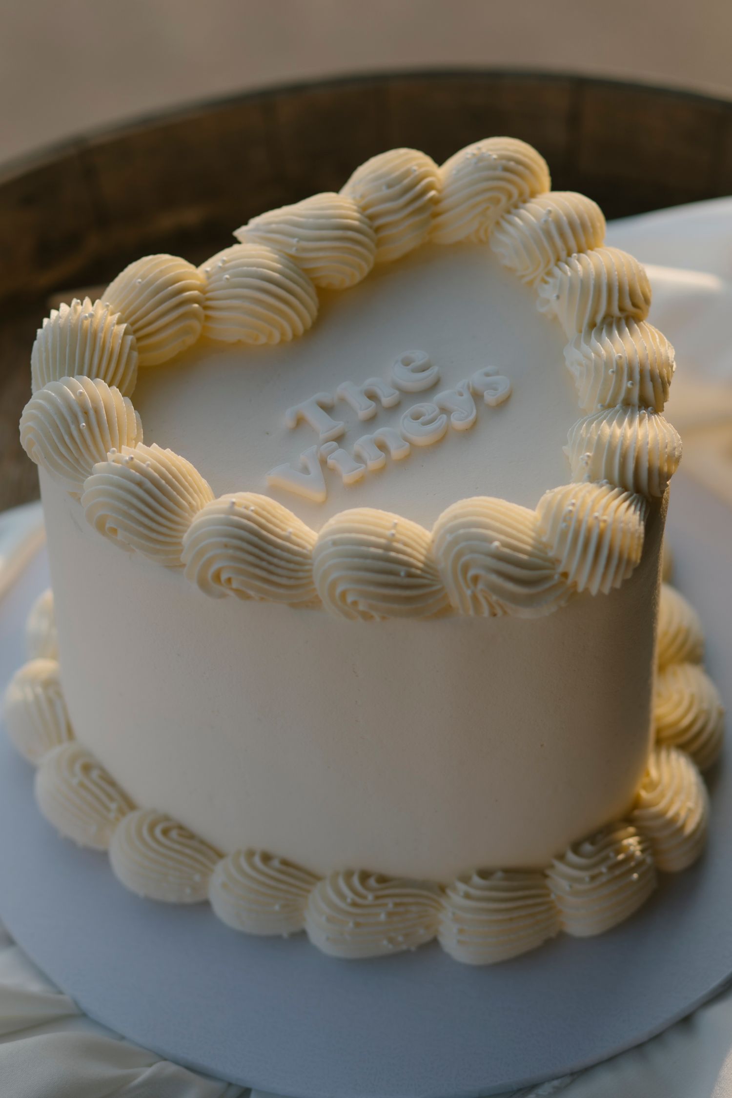 Elegant white wedding cake with cream rosette piping and The Viners text decoration on a cake stand.