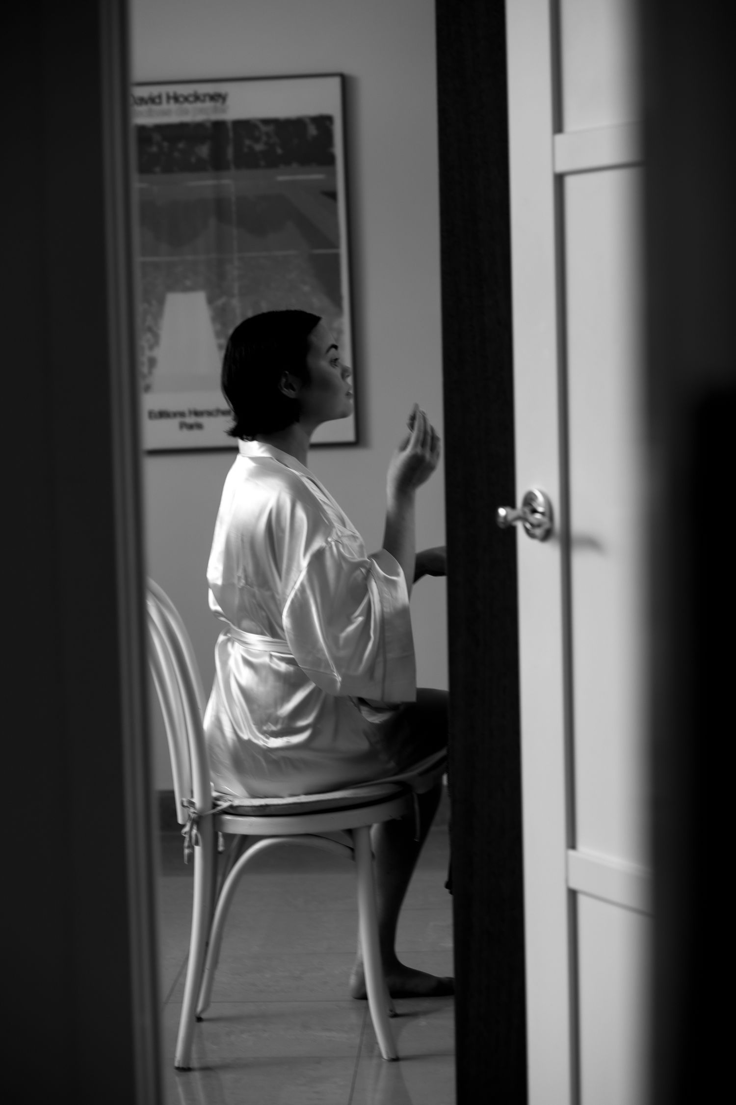 Bride in silk robe sits on chair in black and white getting ready photo.