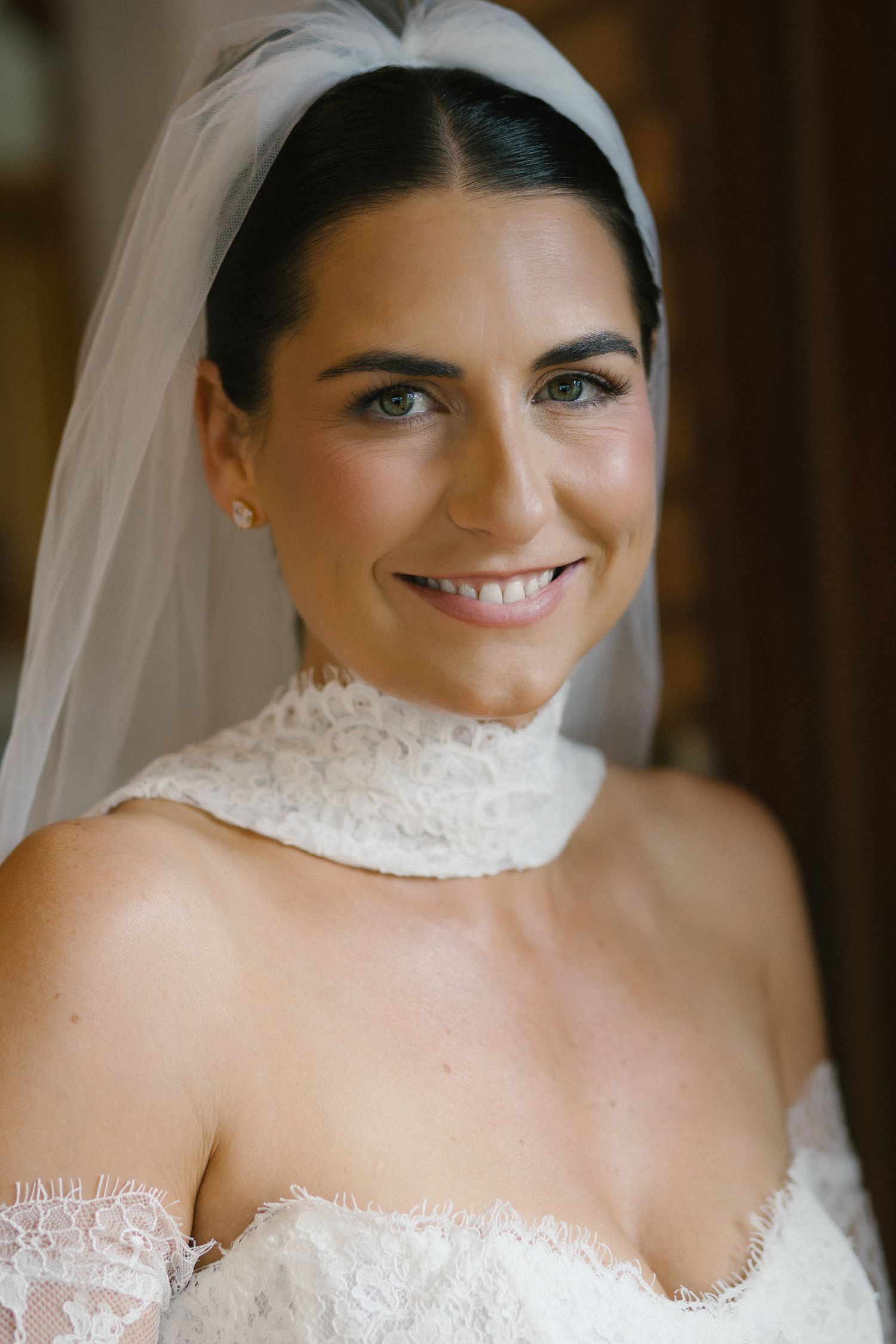 Beautiful bride smiling in a lace off-shoulder wedding gown with a white veil and elegant updo hairstyle.