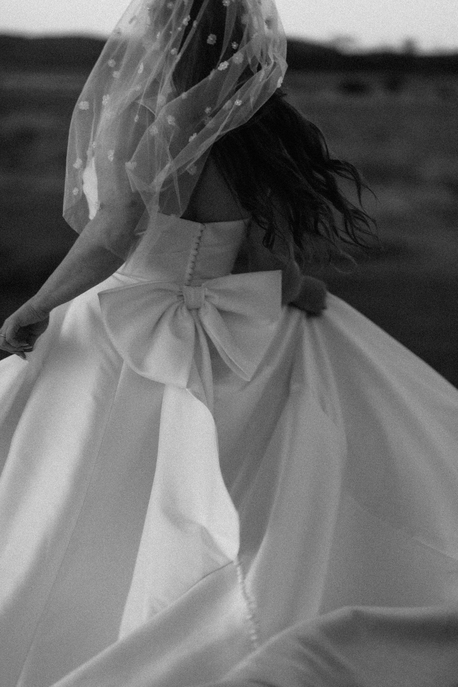 Black and white photo of bride in ball gown with large bow and polka dot veil.