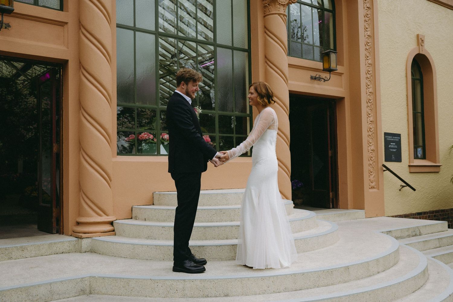 Bride and groom holding hands on steps outside an elegant building on their wedding day.