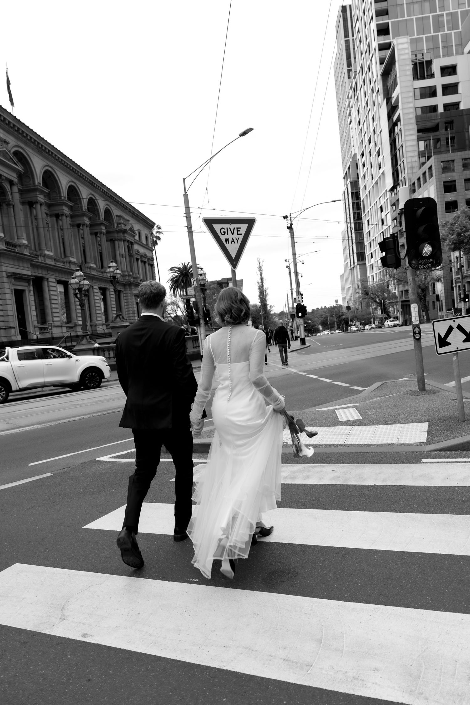 Black and white photo of bride and groom crossing a city street at a crosswalk.