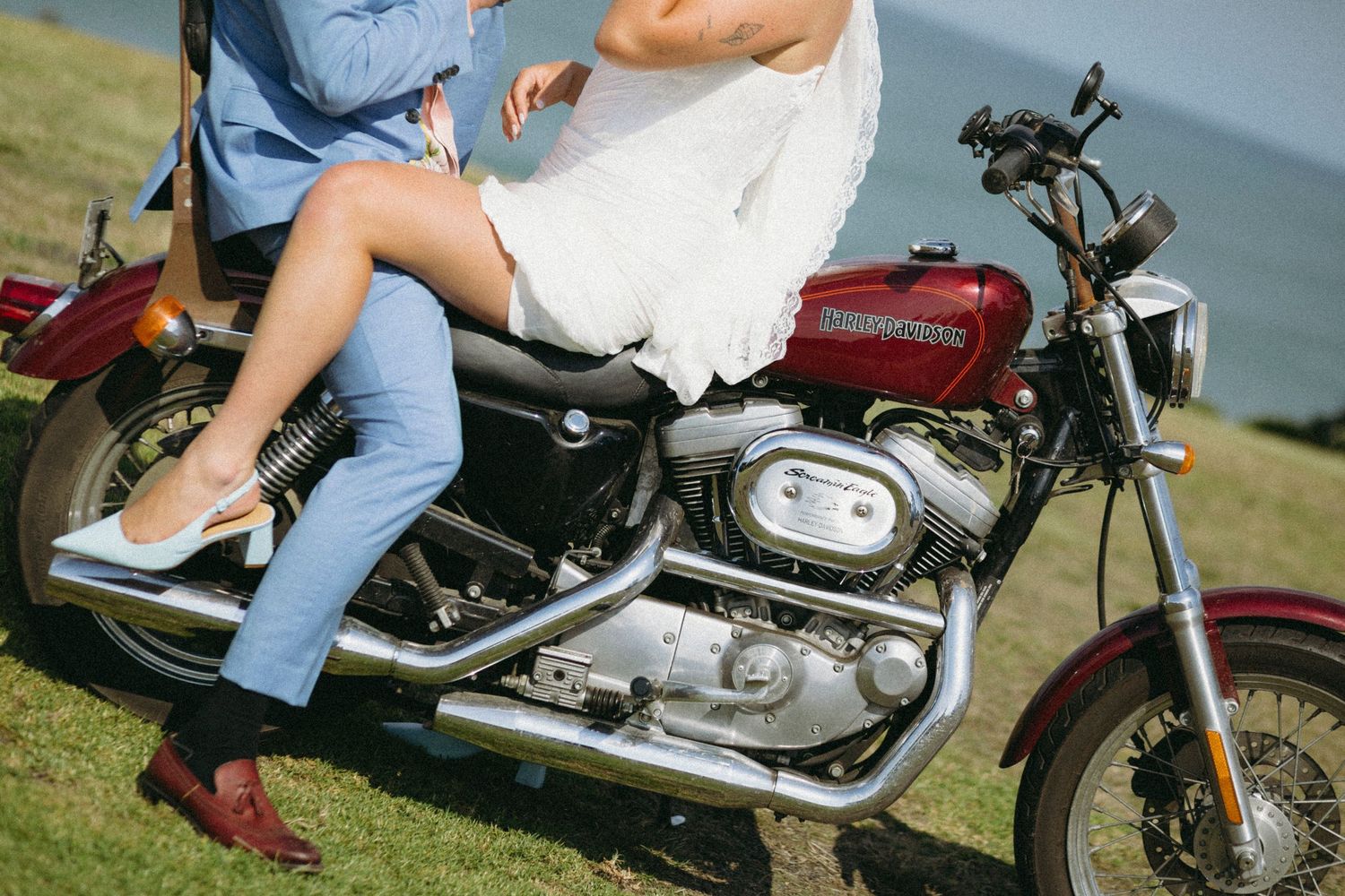 Couple in wedding attire sitting together on a red Harley-Davidson motorcycle outdoors.