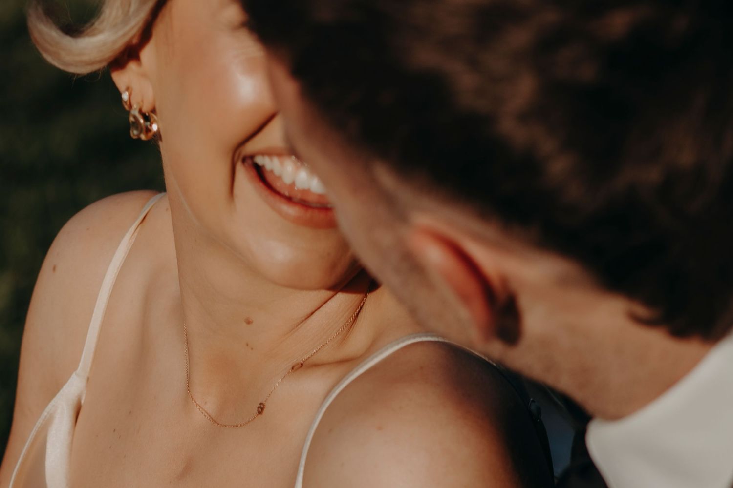 Bride laughs joyfully as groom leans in close during outdoor wedding portraits.