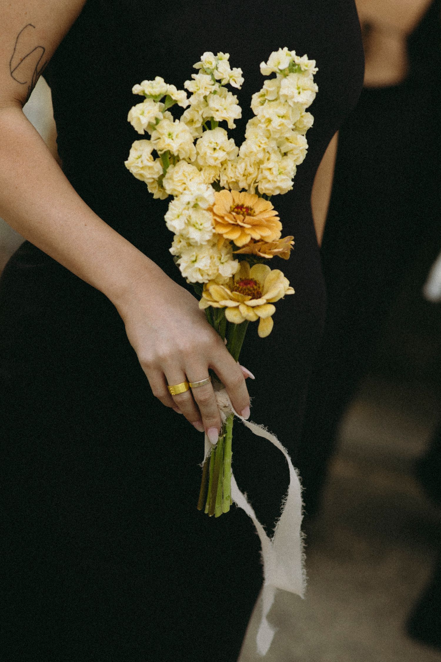 Bridesmaid in black dress holding elegant bouquet of white stock flowers and yellow zinnias.