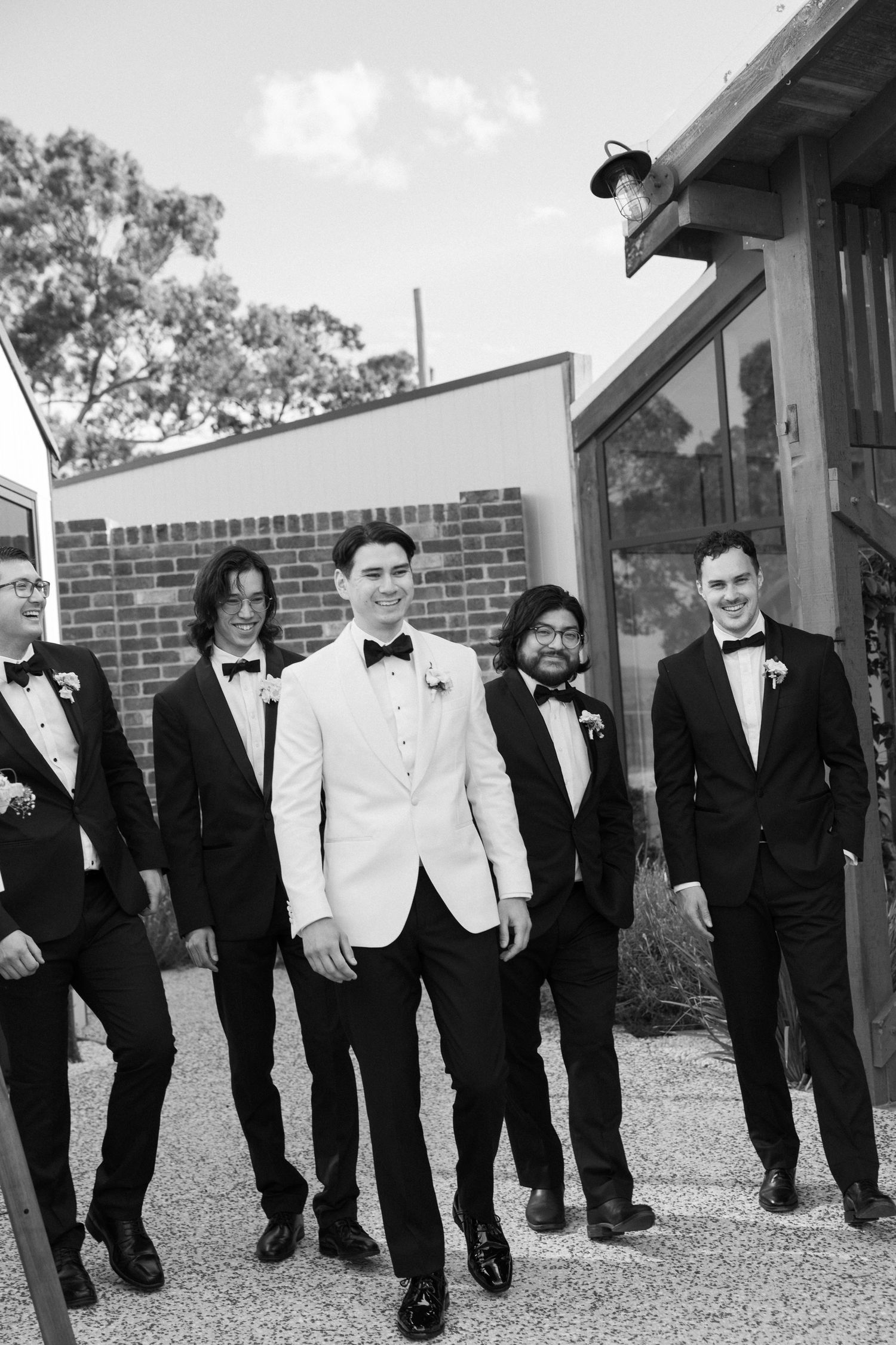 Black and white photo of groom in white jacket walking with groomsmen in black tuxedos.
