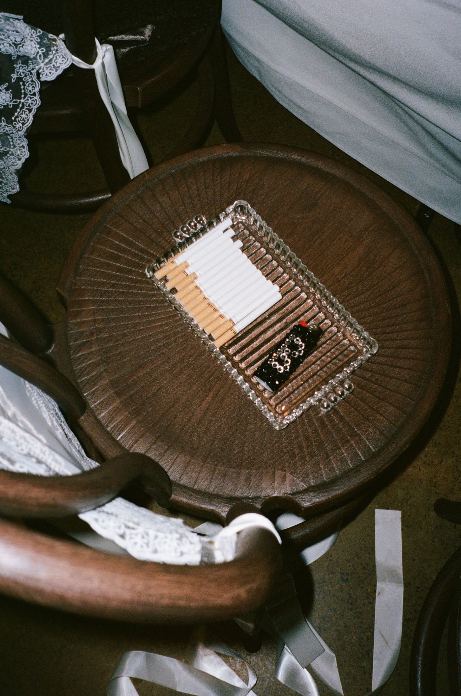 Overhead view of cigarettes and a lighter in a glass ashtray on a round wooden bentwood chair.