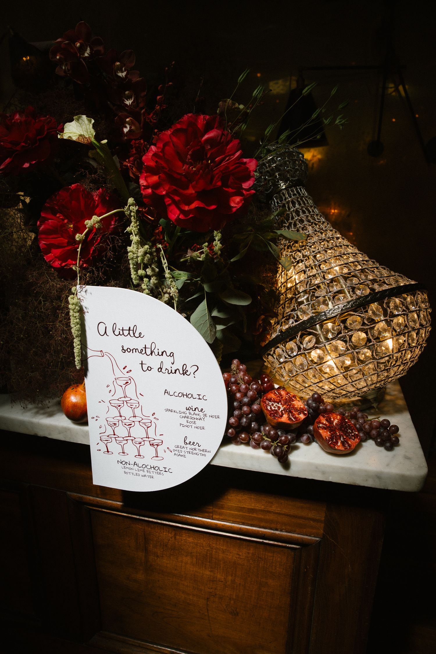 Wedding bar menu card beside red dahlia flowers and a glowing pineapple lamp on marble.