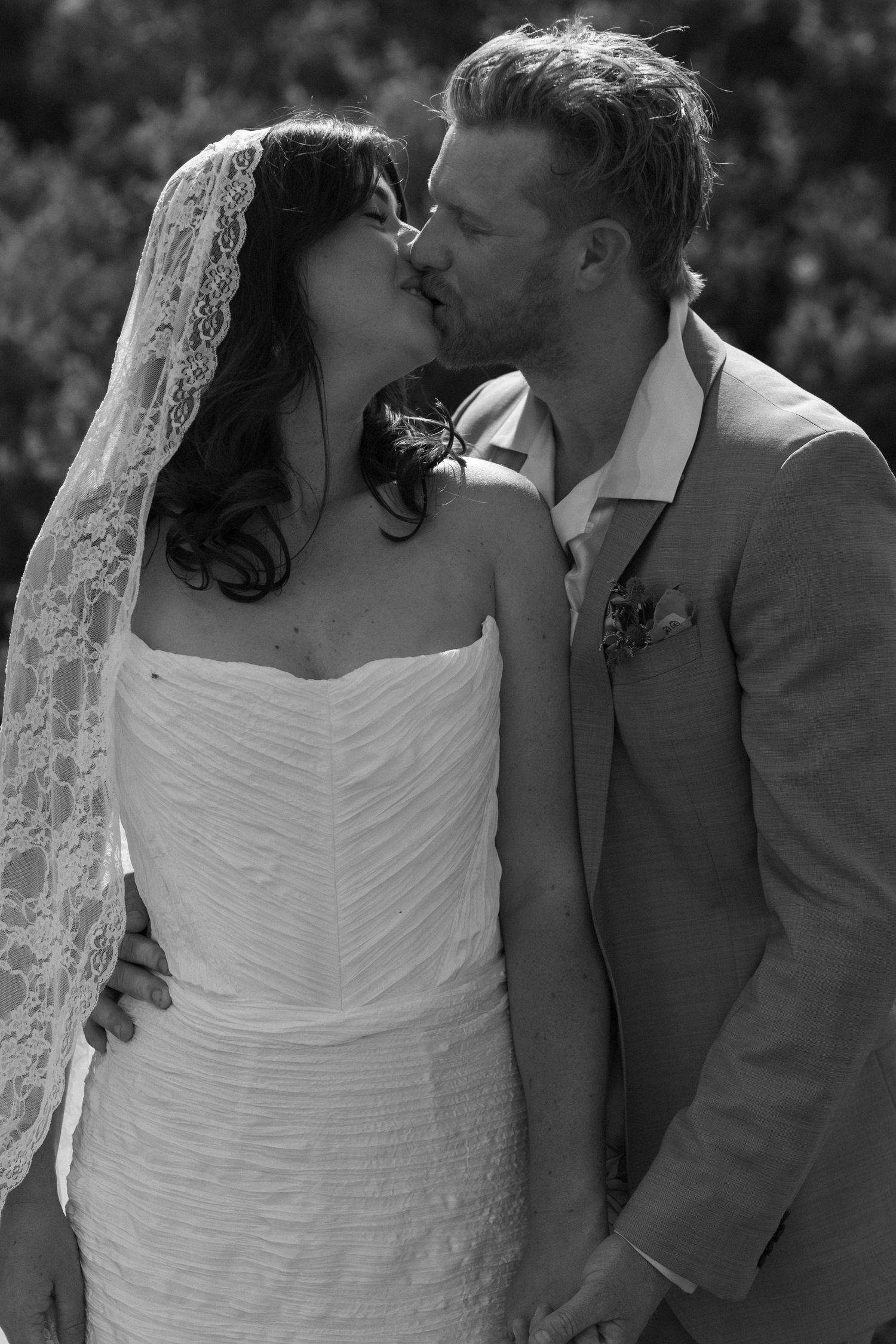 Black and white photo of a bride and groom sharing a kiss, bride wearing lace veil and strapless gown.