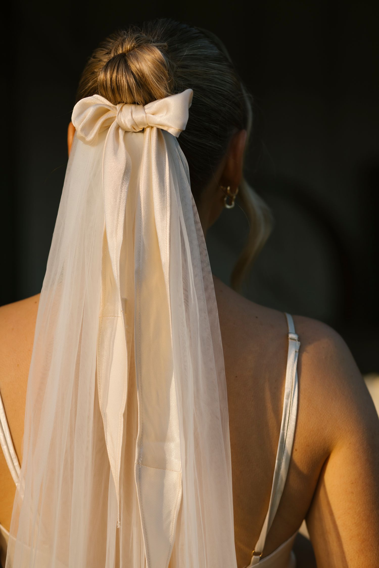 Close-up back view of bride's elegant updo with silk bow and flowing white veil.