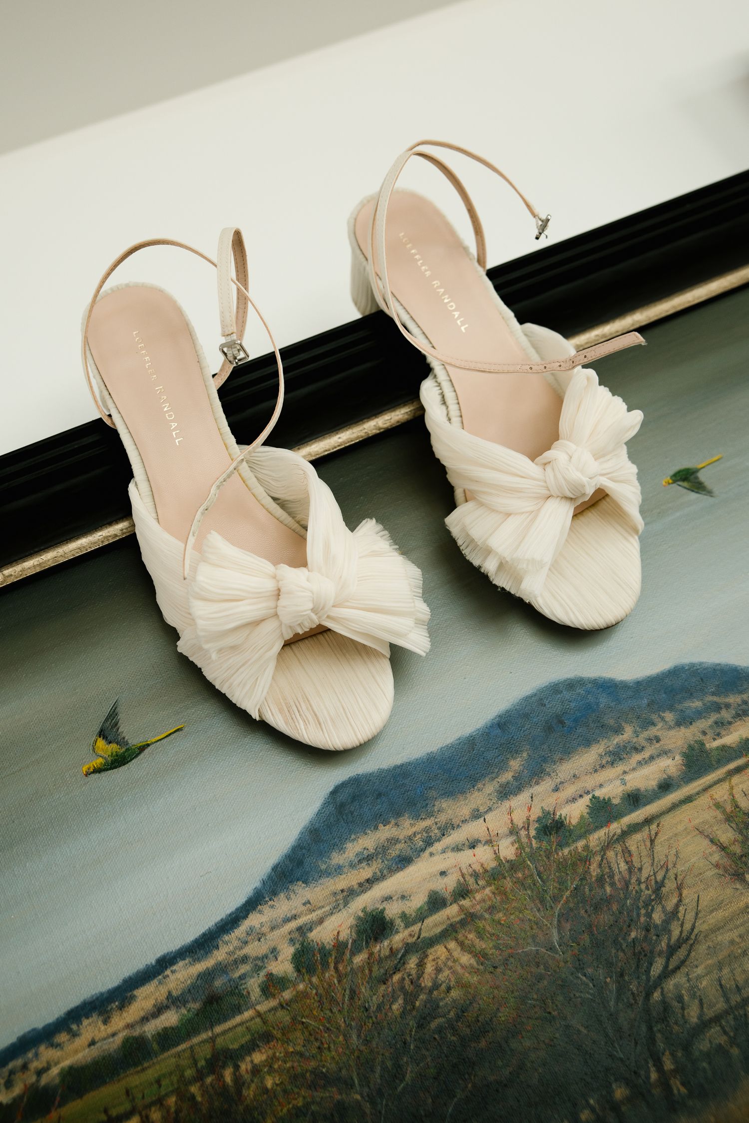 Elegant ivory bridal heels with tulle bow detail displayed on a painted decorative surface.