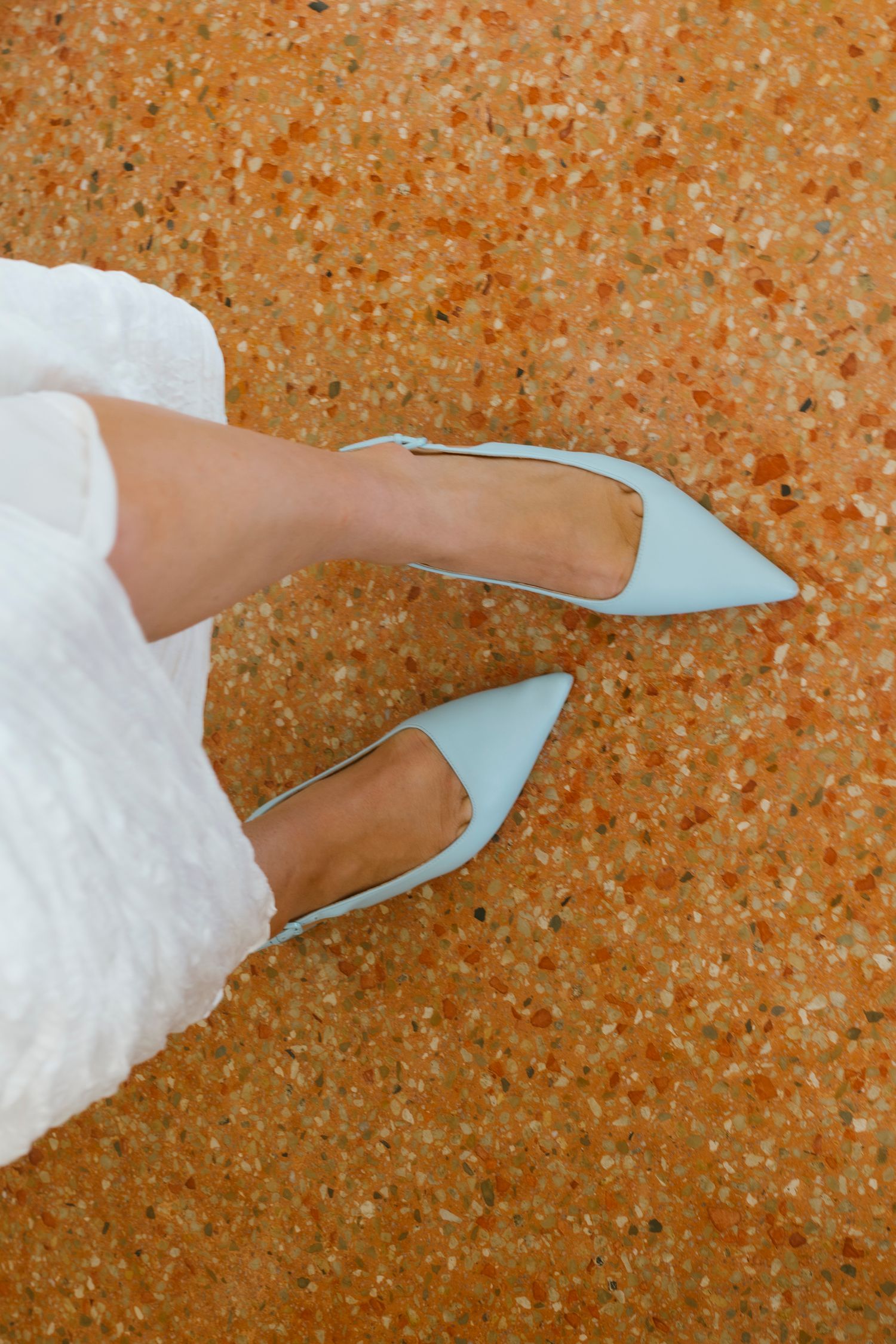 Close-up of bride wearing light blue pointed-toe heels against a terrazzo floor background.