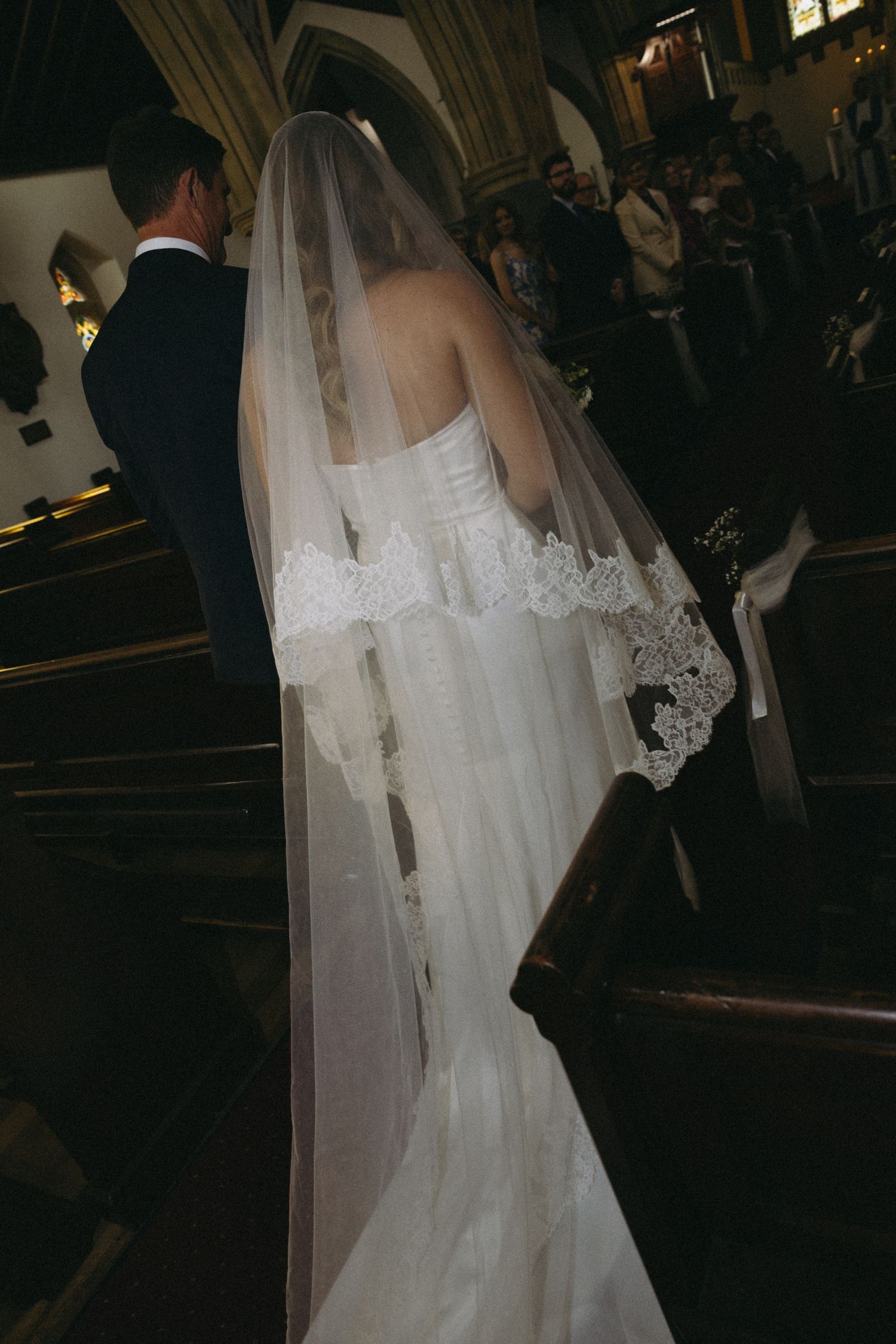 Bride in lace-trimmed cathedral veil and fitted gown walking down church aisle with groom.