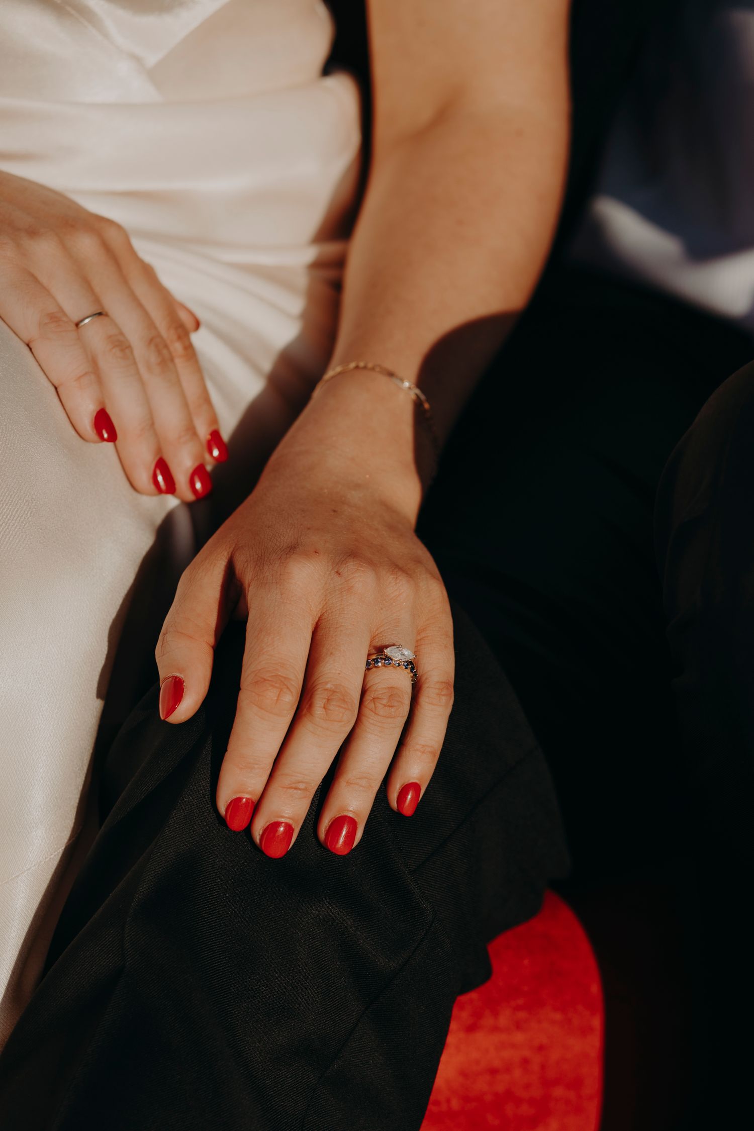 Close-up of bride and groom hands with red nails, diamond engagement ring, and gold bracelet.