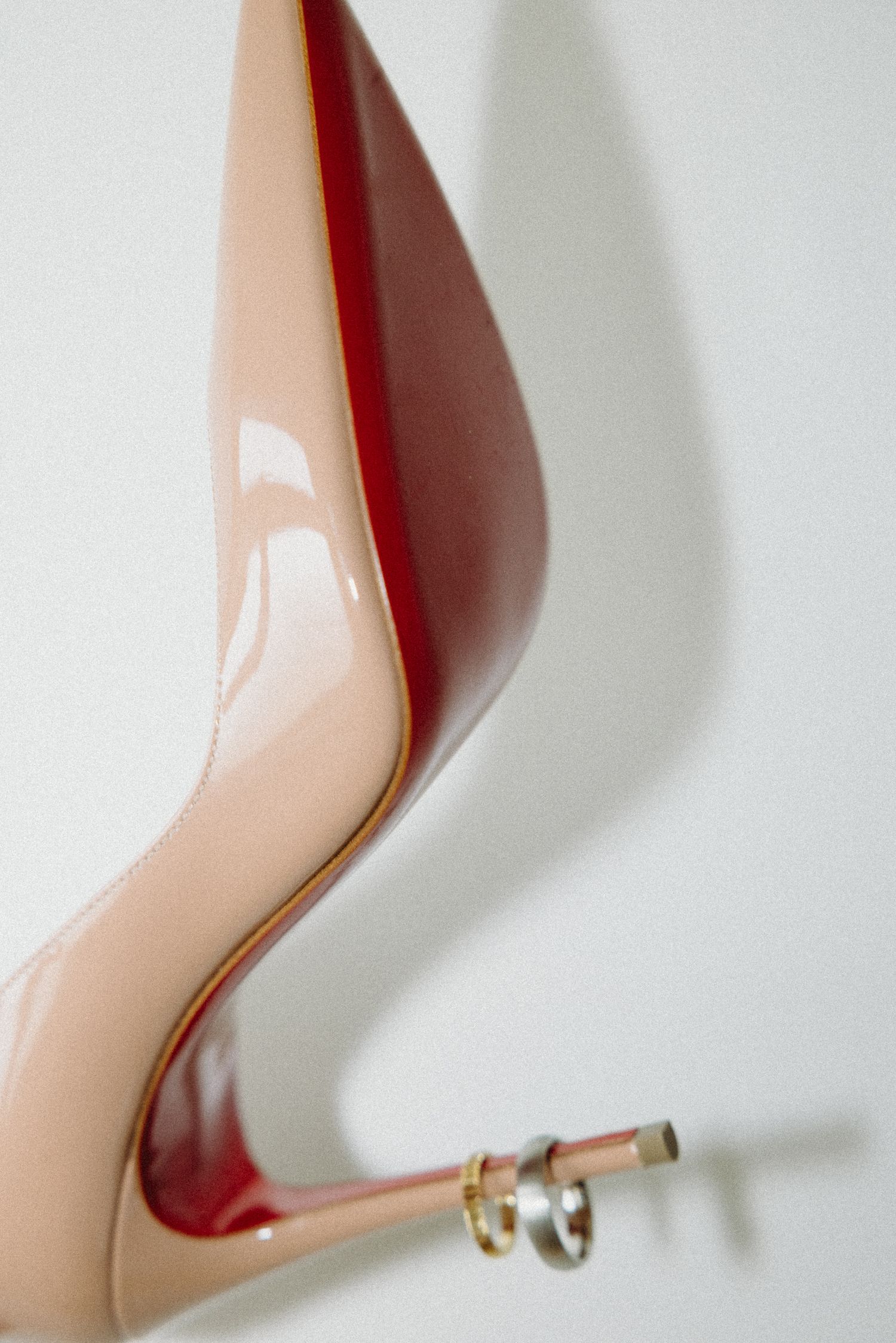 Nude patent leather Christian Louboutin stiletto heel with red sole and wedding rings resting on the heel.