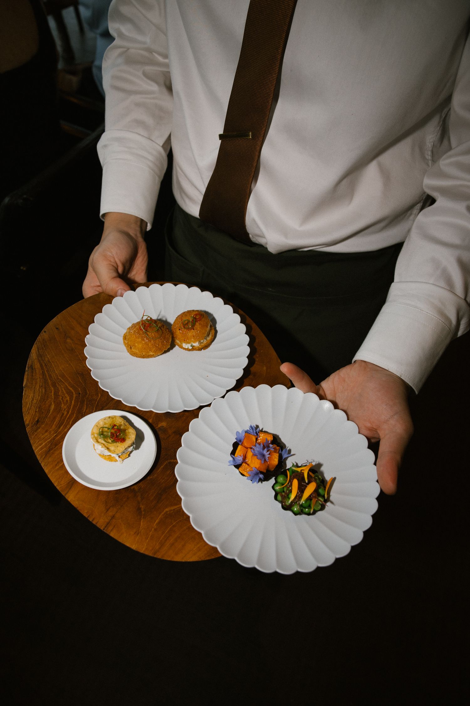 Waiter presenting elegant white scalloped plates with gourmet appetizers at a wedding reception dinner.