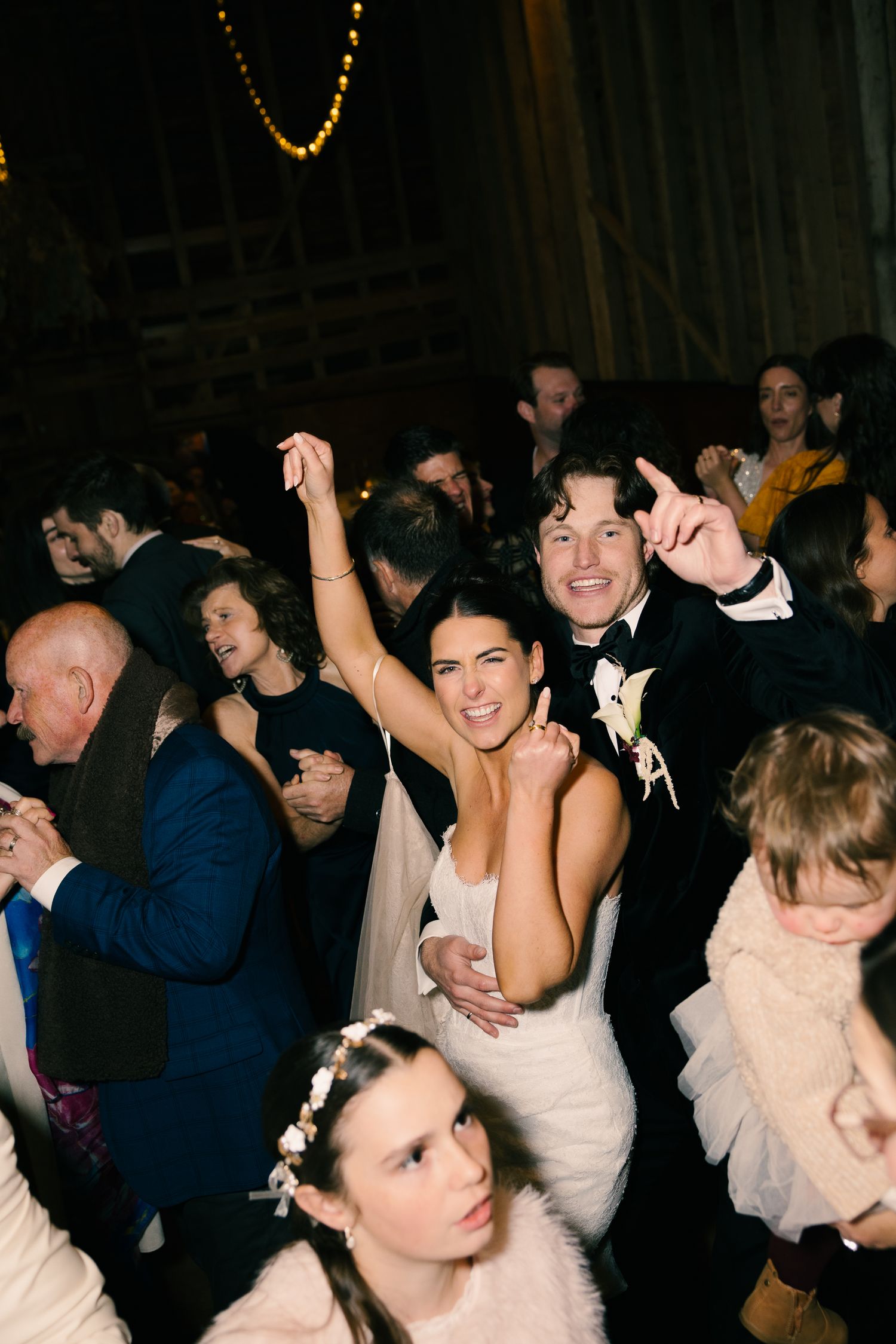 Joyful bride and groom dancing together with wedding guests on a lively reception dance floor.