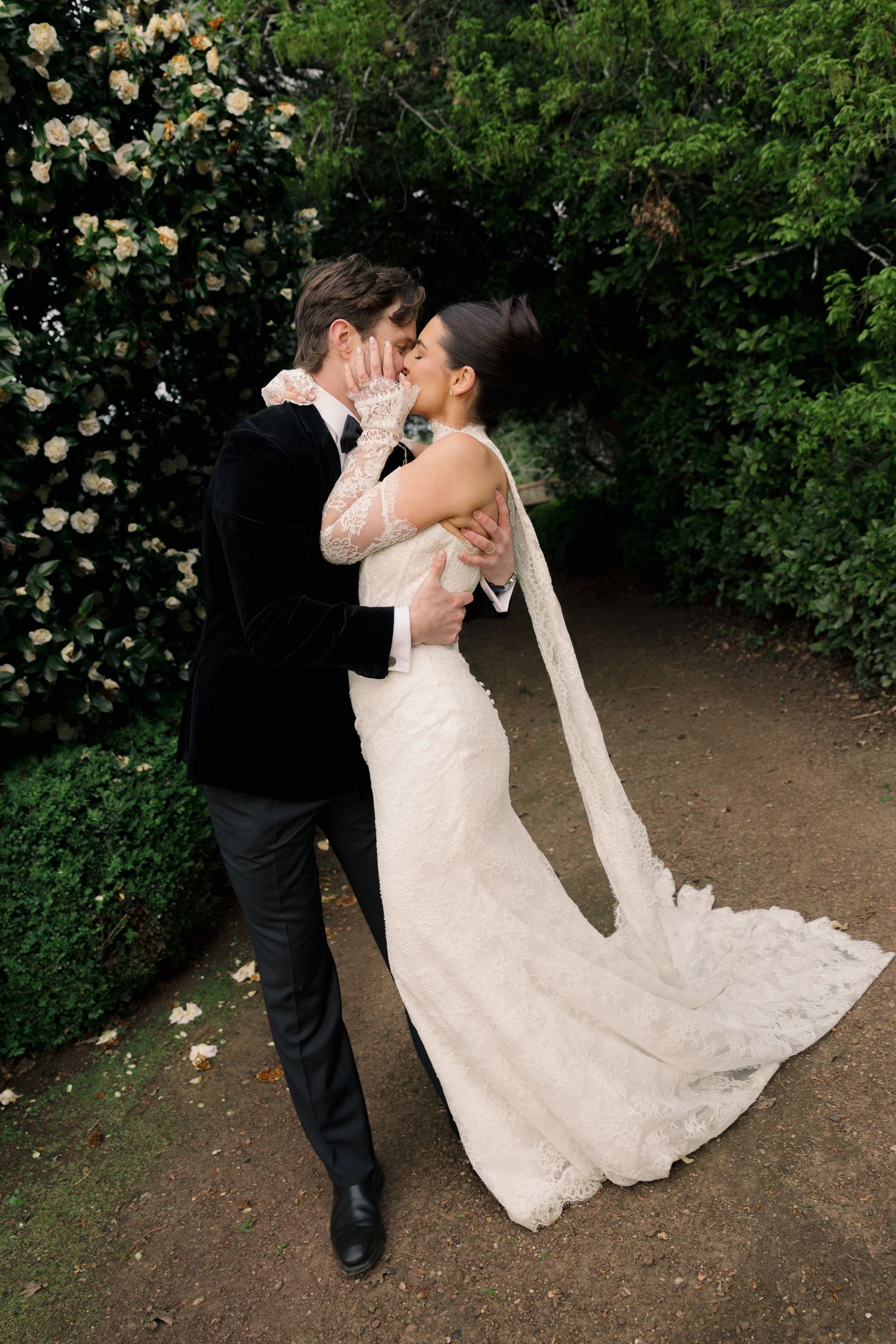 Bride and groom sharing a romantic kiss on a garden path surrounded by lush greenery.