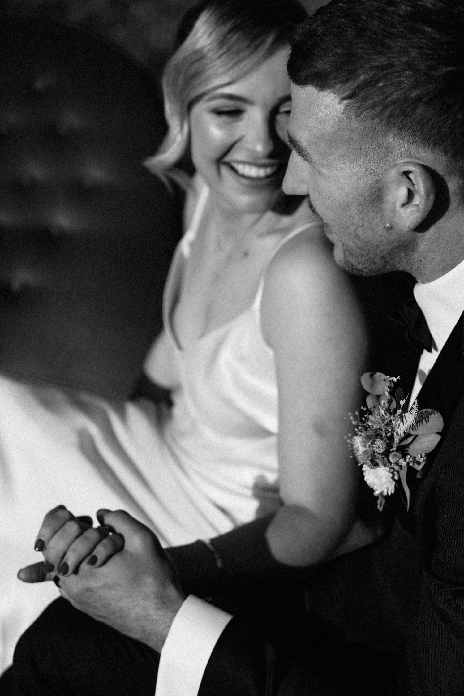 Bride and groom hold hands and laugh together in black and white wedding portrait.