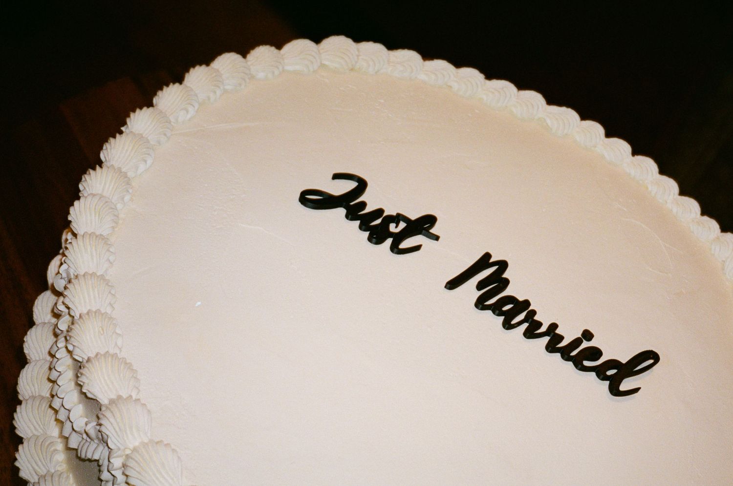 White wedding cake with decorative piped border and elegant black cursive Just Married text on top.