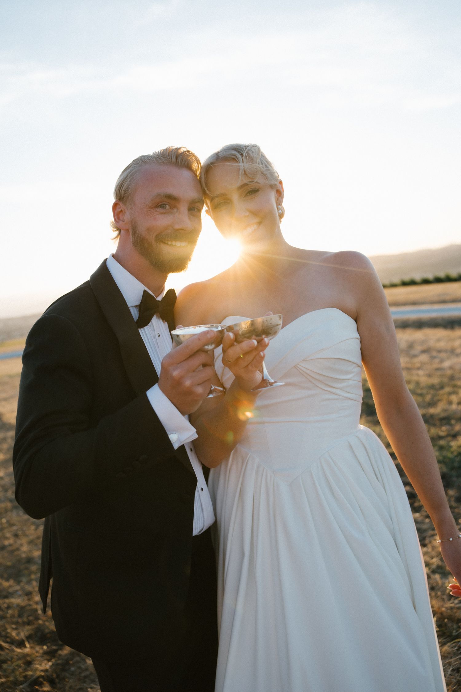 Bride and groom toasting with champagne at golden hour in an open field at sunset.