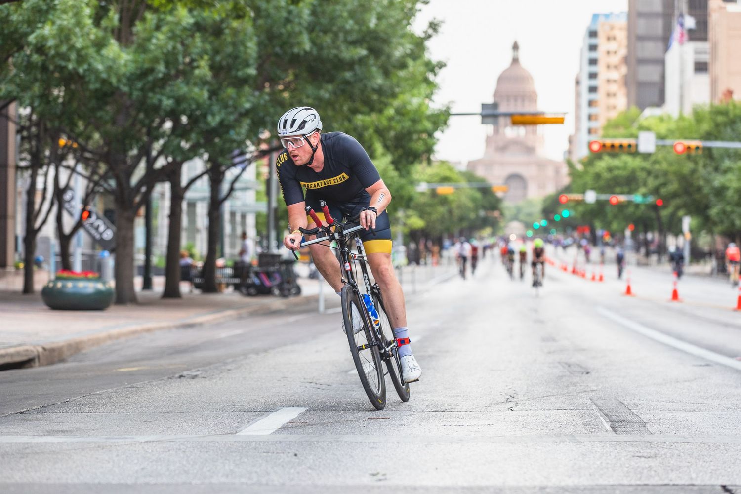 Cyclist riding road bike down a wide urban street with the Texas State Capitol building visible in background.