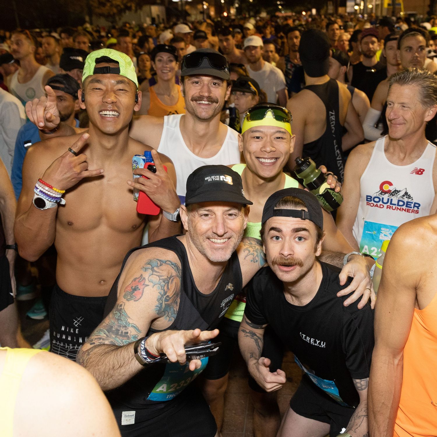 Group of smiling male runners posing together at nighttime race event wearing athletic gear.