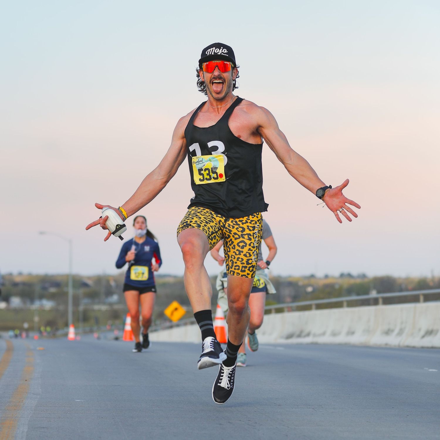 Energetic male runner in leopard print shorts and tank top jumping during a road marathon race.