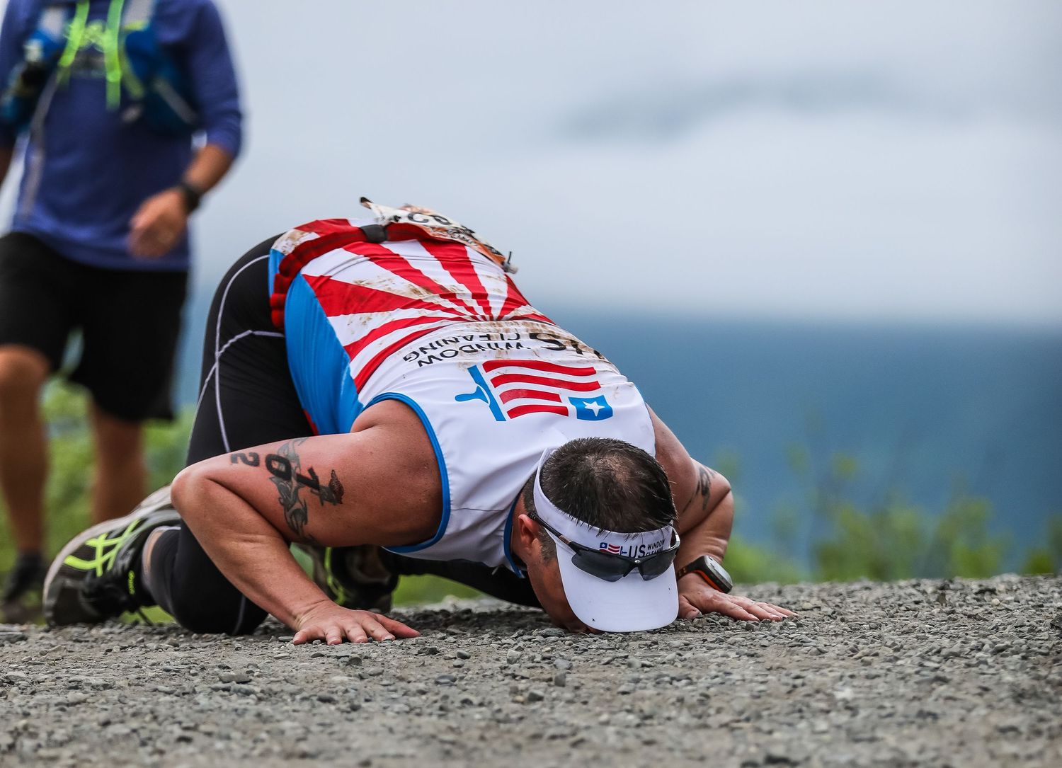 Exhausted triathlete kisses ground after completing grueling mountain race at finish line.