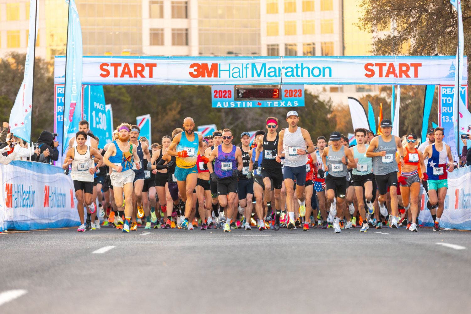 Runners start the 3M Half Marathon race in Austin, Texas, beneath a large START banner on a city street.