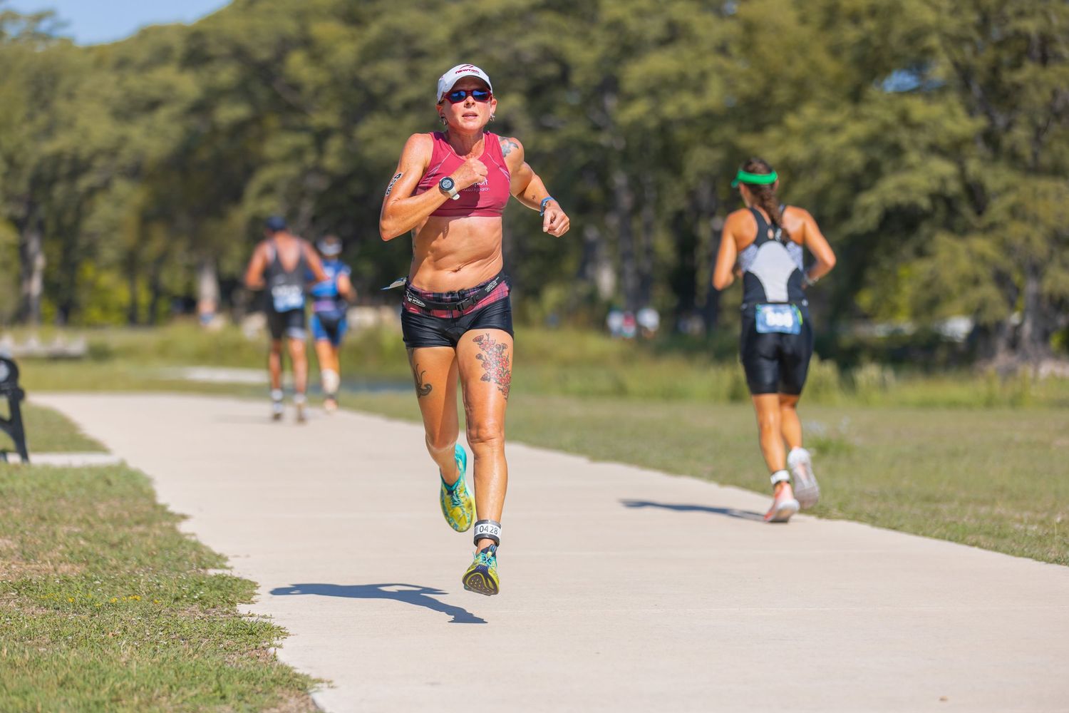 Female triathlete in athletic wear runs along a paved path during a sunny outdoor triathlon race.