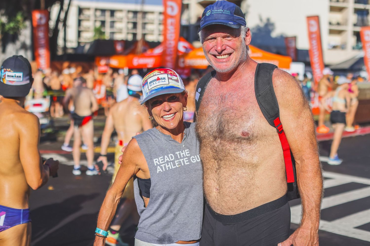 Smiling couple poses together at triathlon start area, woman wearing Read the Athlete Guide visor.