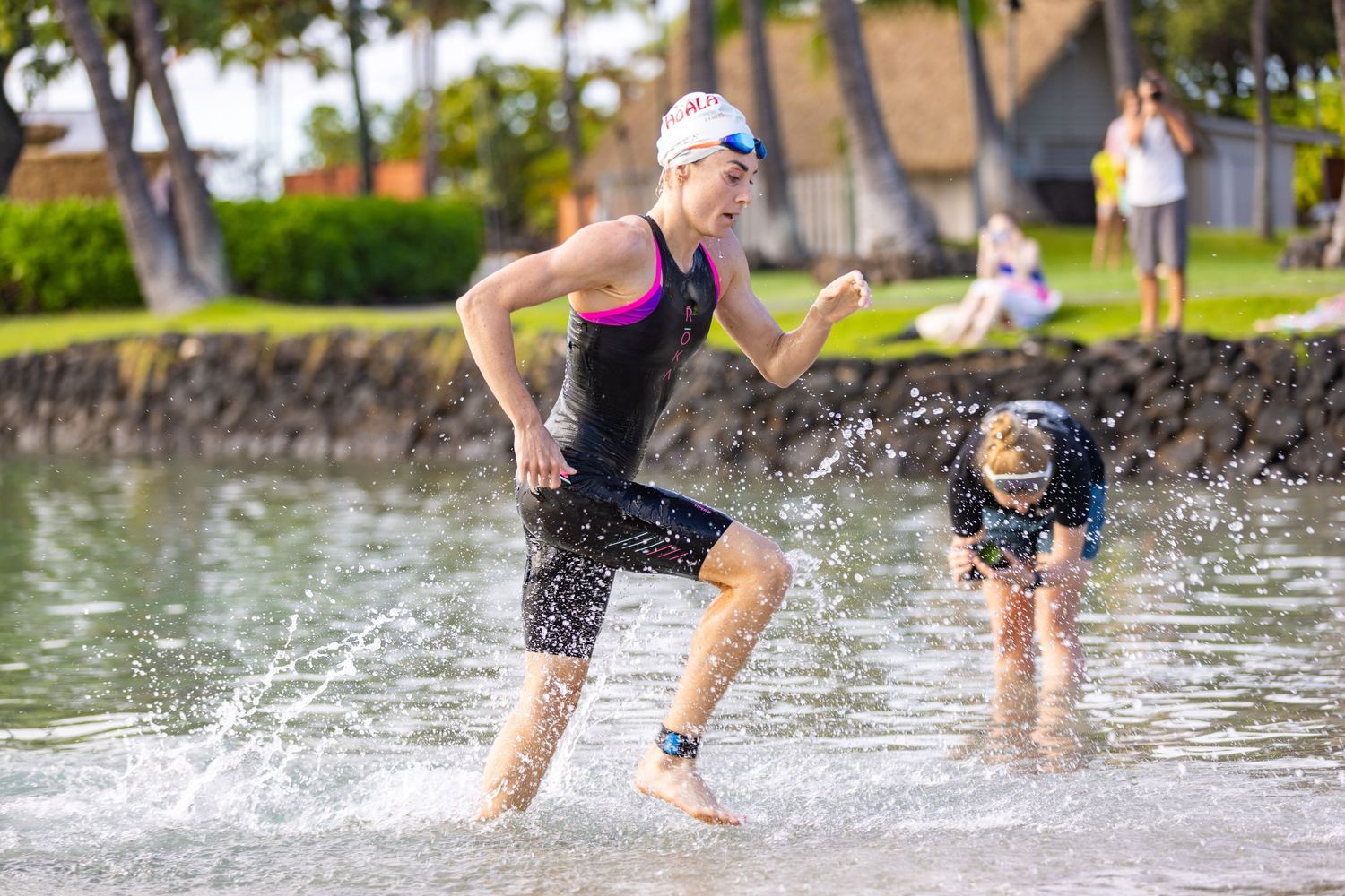 Female triathlete running out of water wearing wetsuit and swim cap during a triathlon transition in Hawaii.