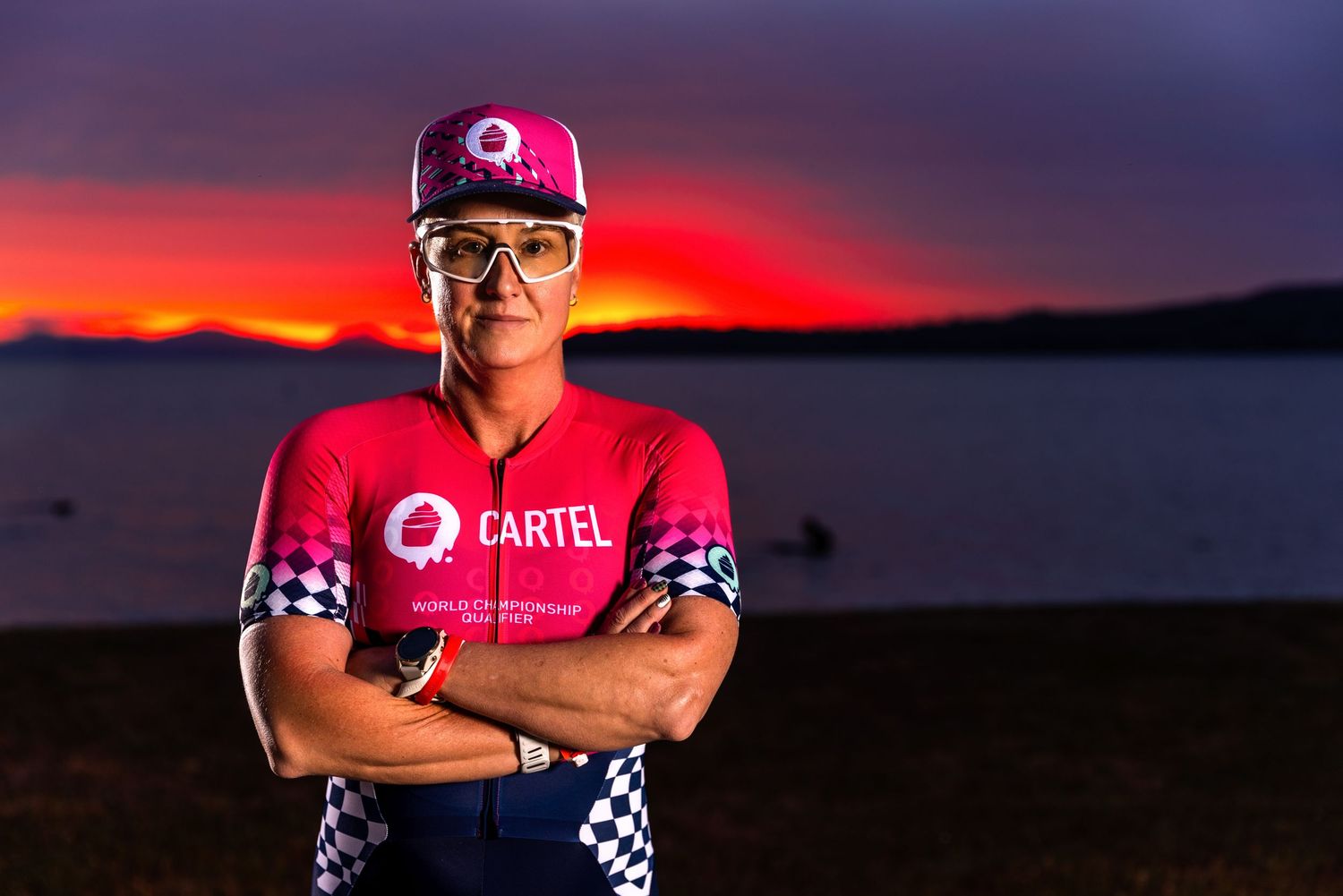 Triathlete portrait at dusk beside Lake Taupō wearing a cycling kit and cap during a dramatic sunset photoshoot.